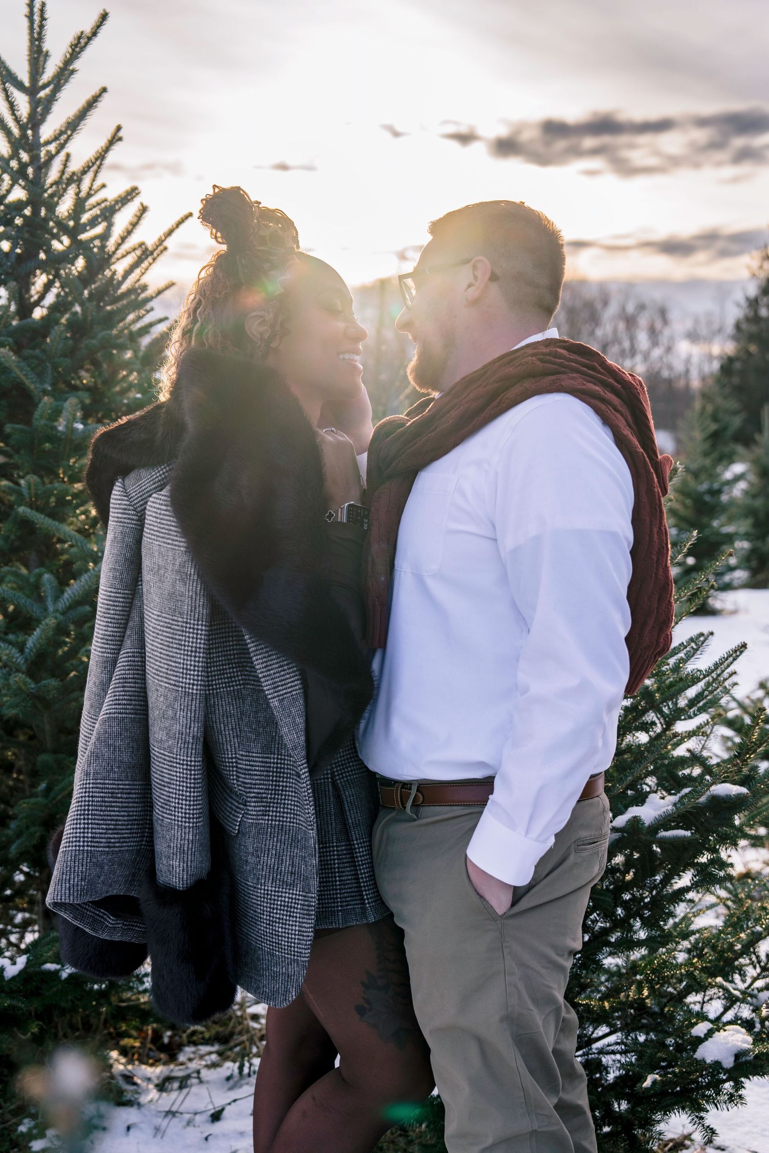 A couple shares an intimate moment among snow-covered evergreen trees at sunset.