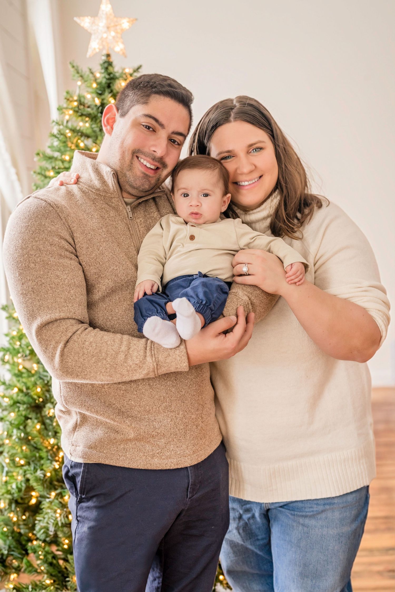 A family poses together in front of a Christmas tree in a series of candid holiday photos. Family photoshoot. Family photography.