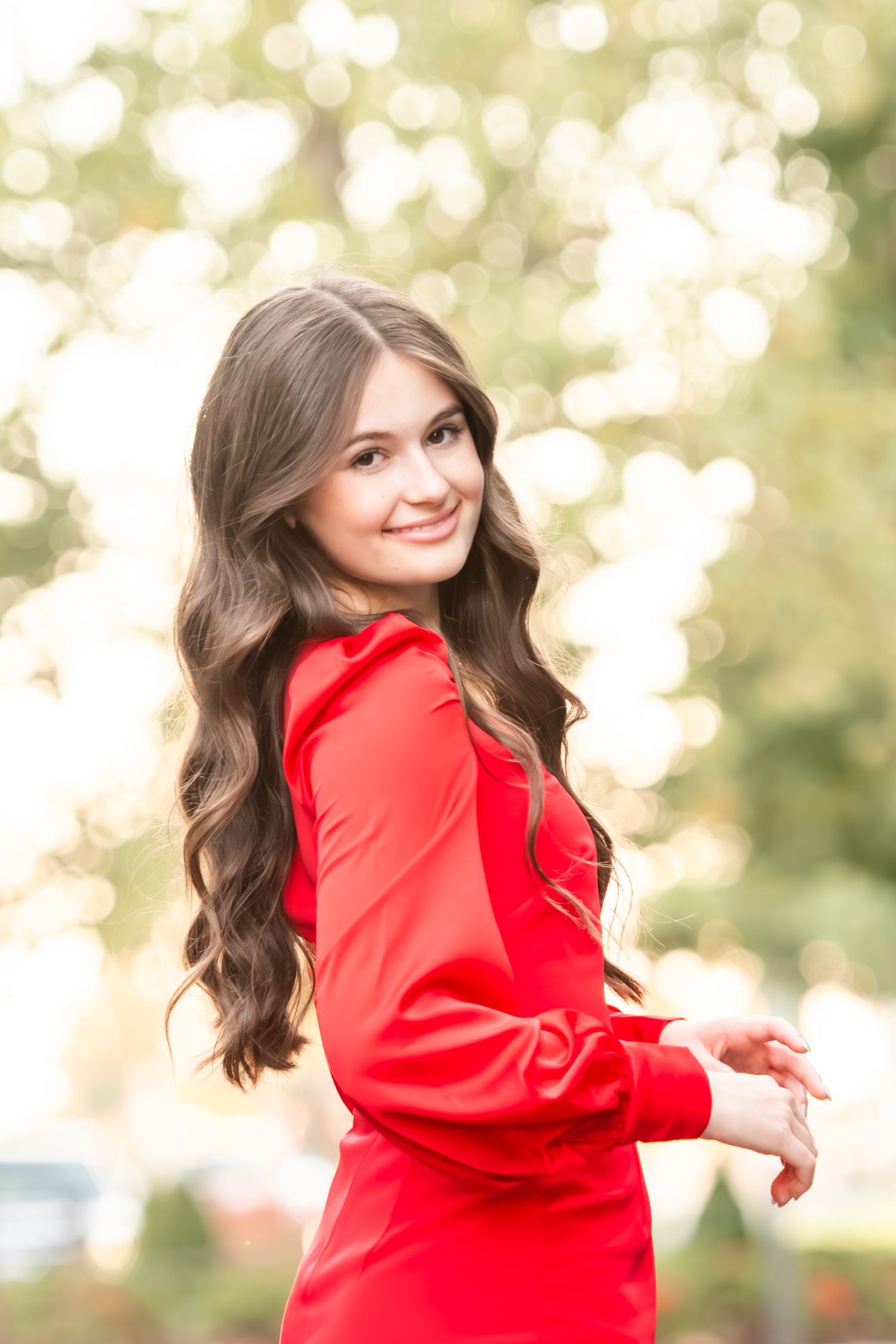Barstow senior photo in bright red dress poses against blurred bokeh background outdoors in Overland Park, KS