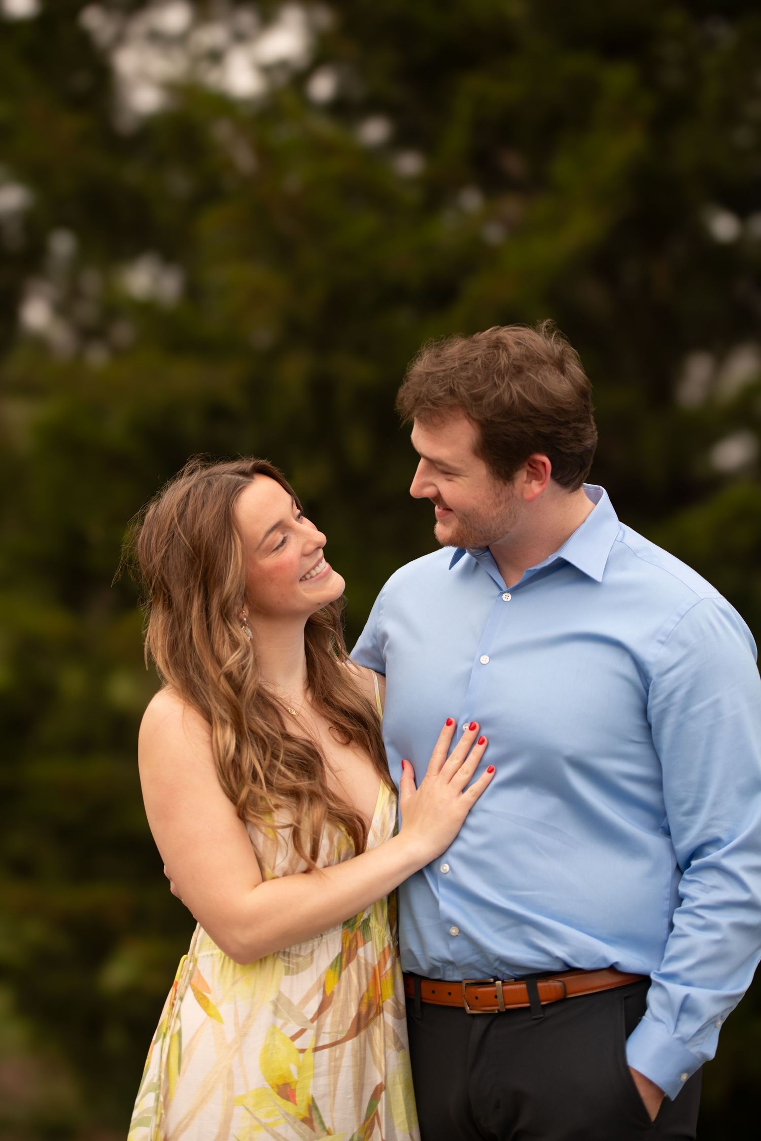 Candid moment captured between couple against evergreen background.