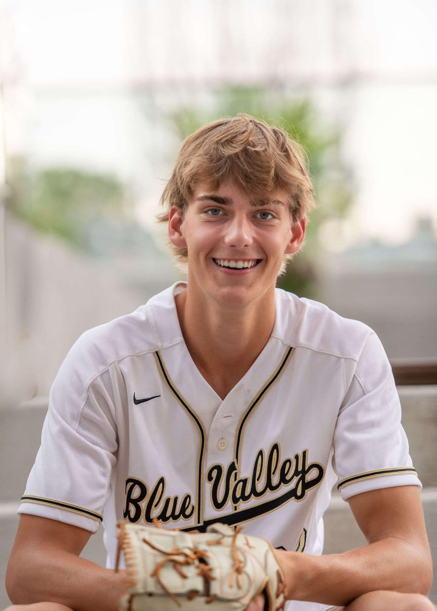 Person in white baseball uniform smiles at camera while wearing Blue Valley jersey.