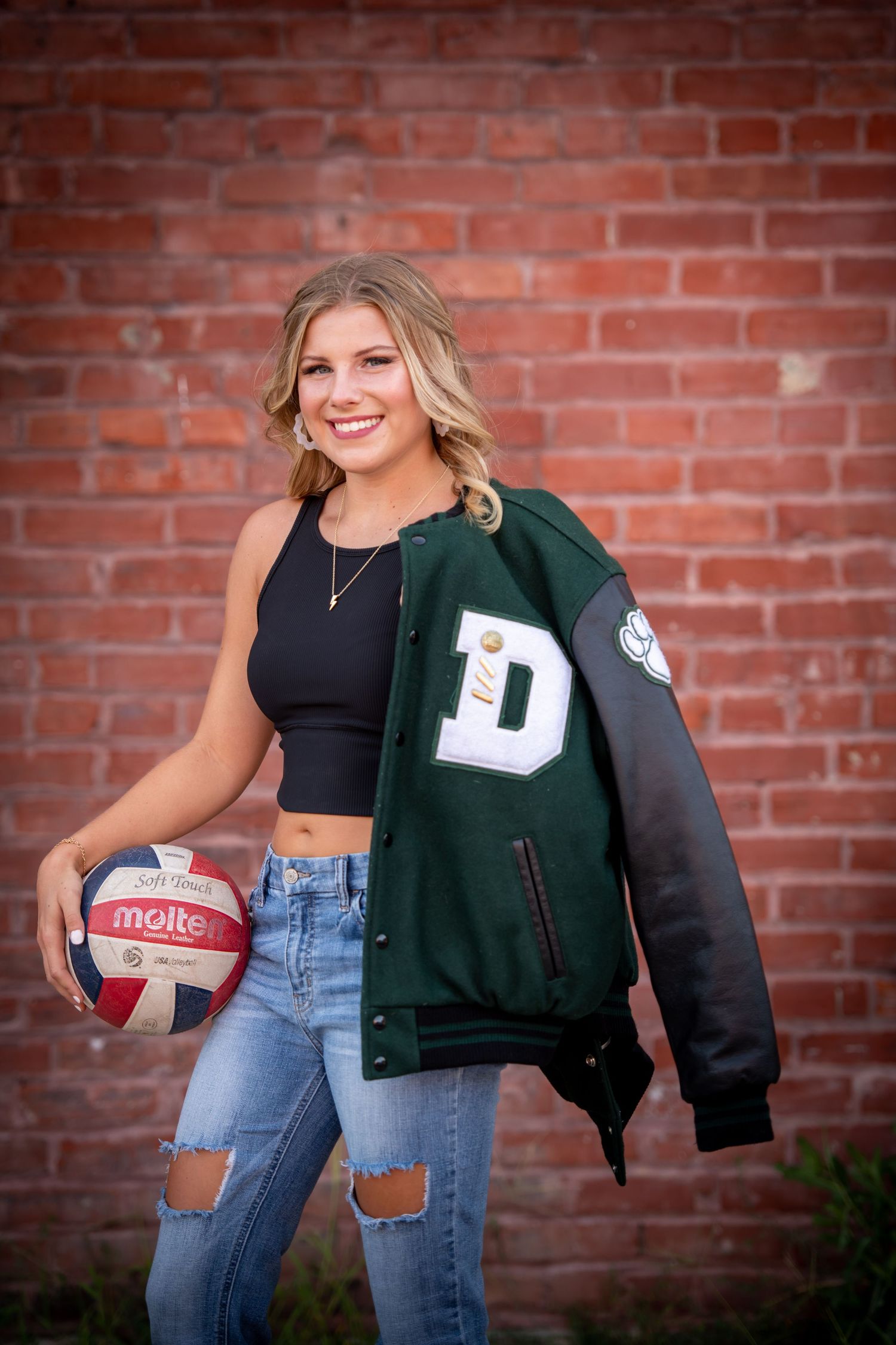 Athletic portrait showing varsity letterman jacket and volleyball against brick wall backdrop.