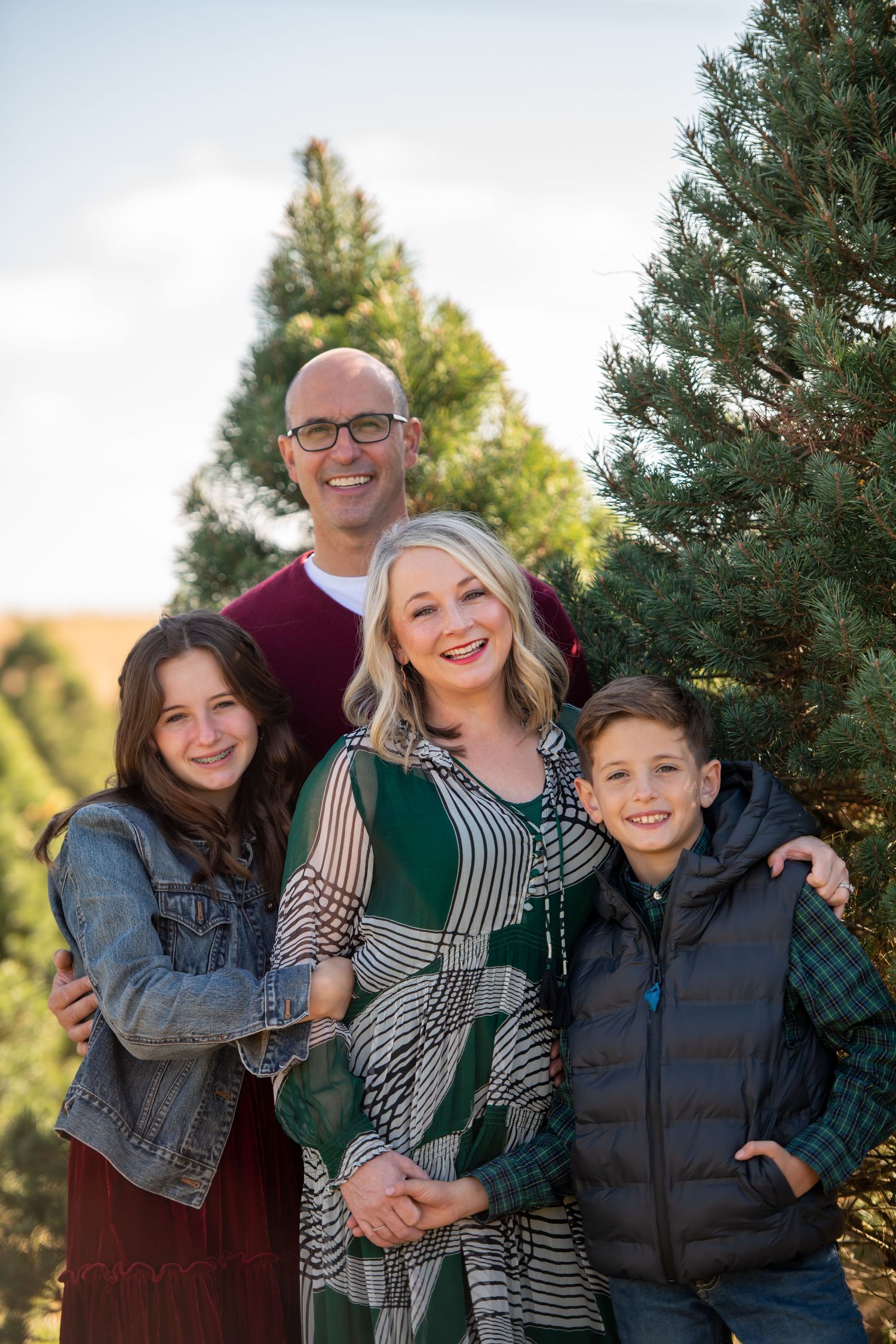 Happy family of four posing together among pine trees in outdoor setting.