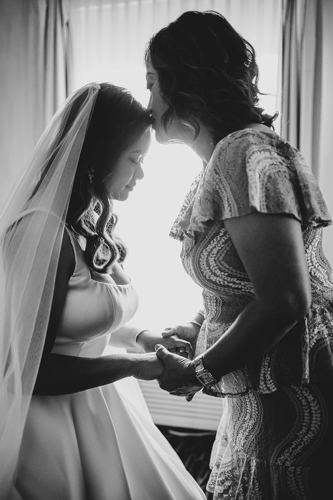 An intimate black and white photo capturing a tender moment between two people in wedding attire.