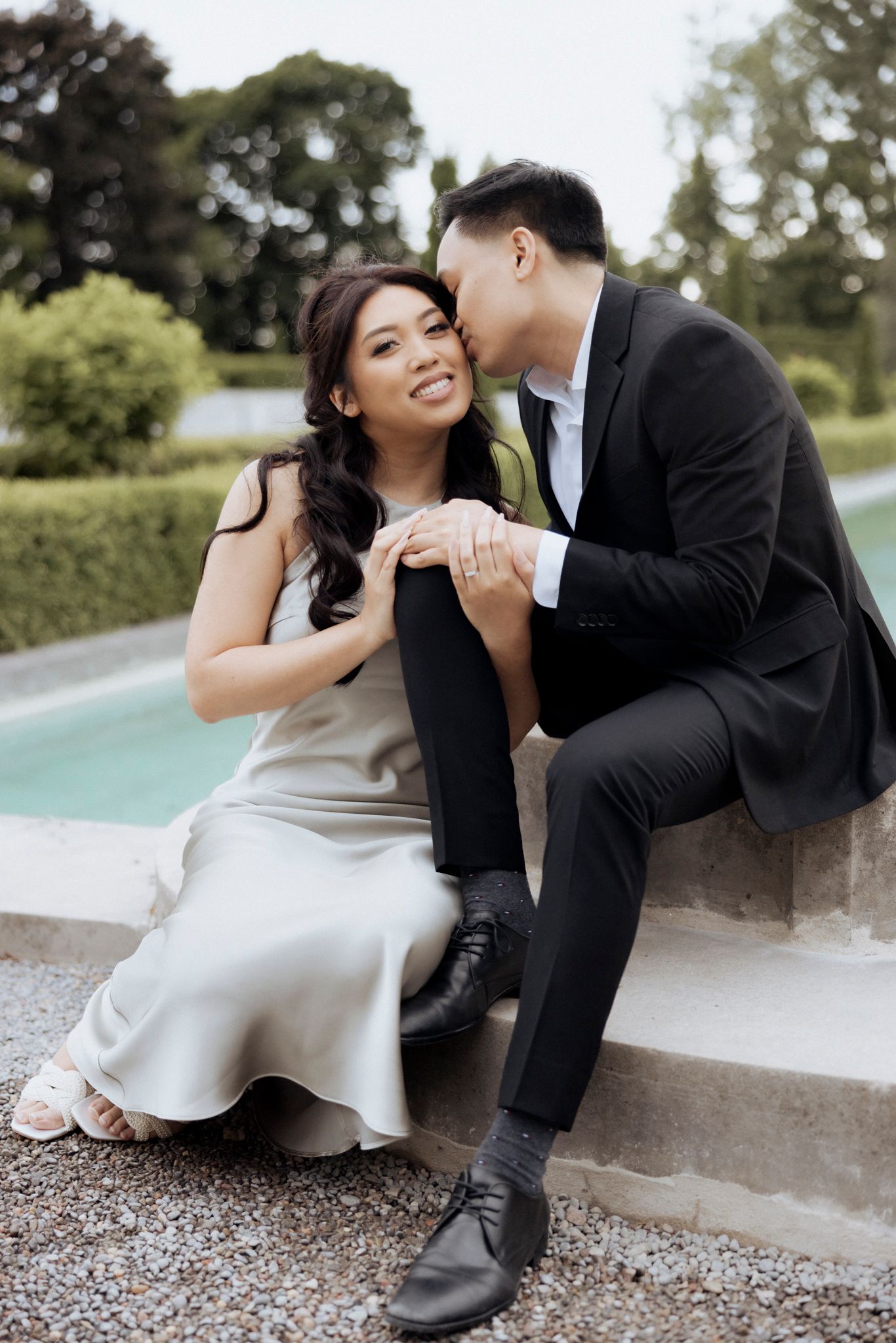 A romantic moment between a couple in elegant attire sitting by a pool.