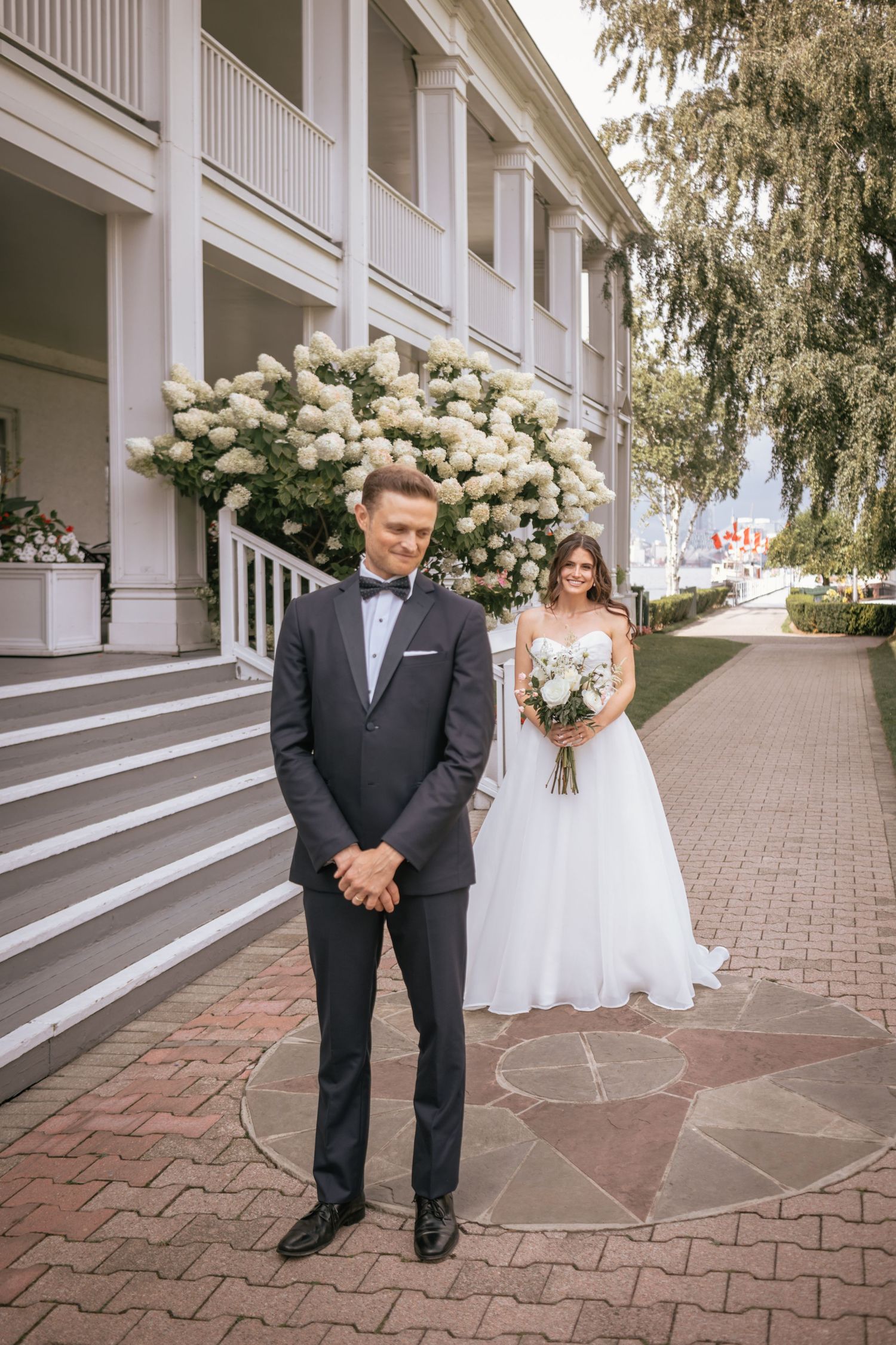 Classic wedding first look moment captured outside historic Southern mansion with white columns and blooming hydrangeas.