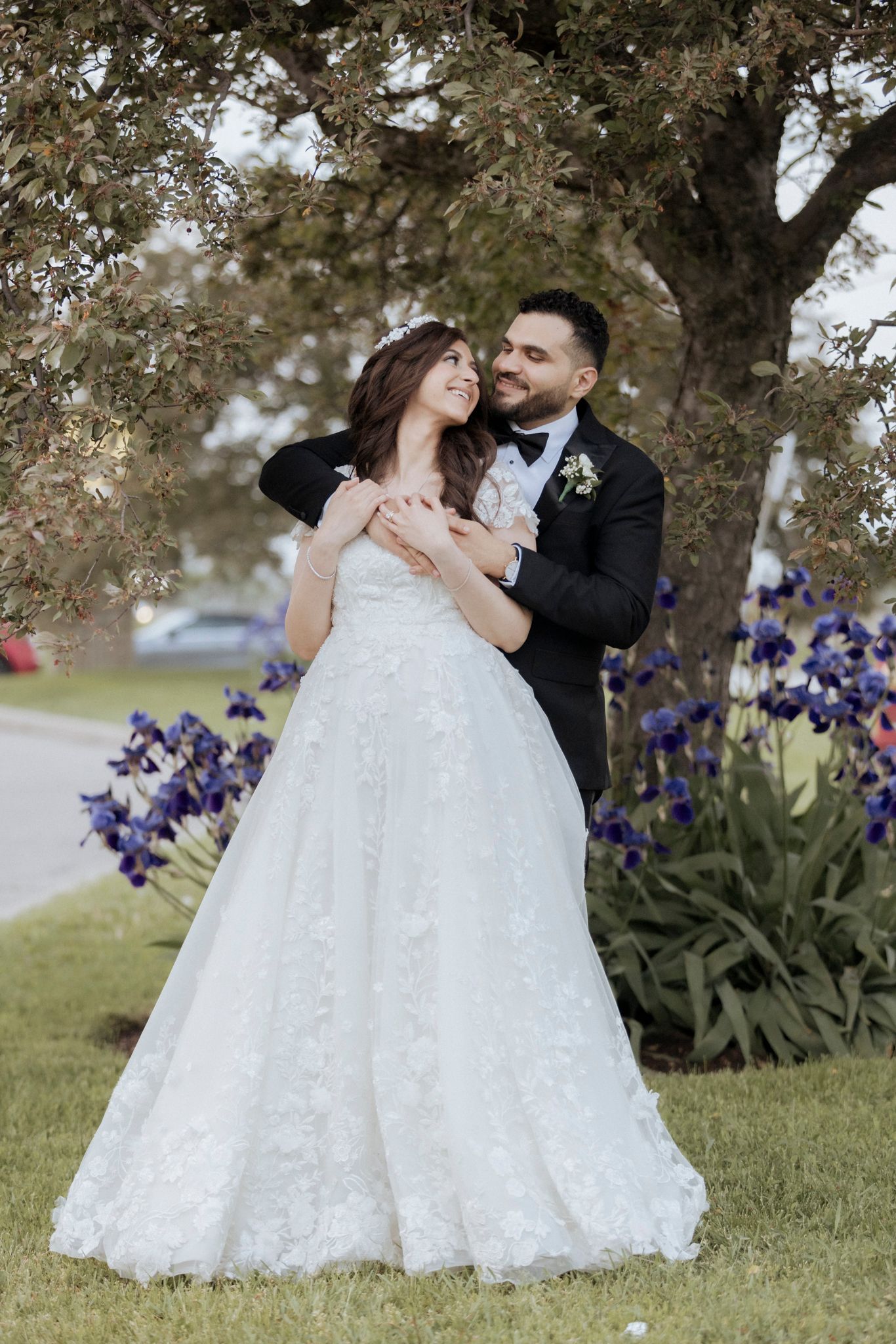 A romantic wedding portrait near purple iris flowers and a large tree.