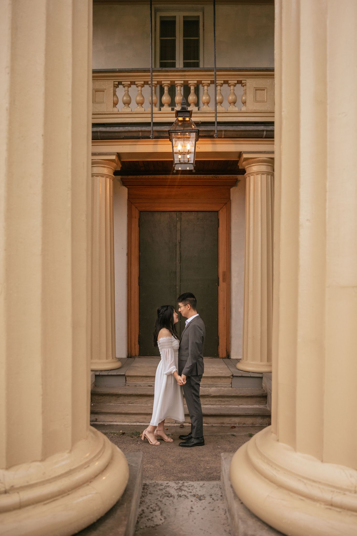 Couple standing between grand cream-colored columns at a historic building entrance with ornate architectural details.