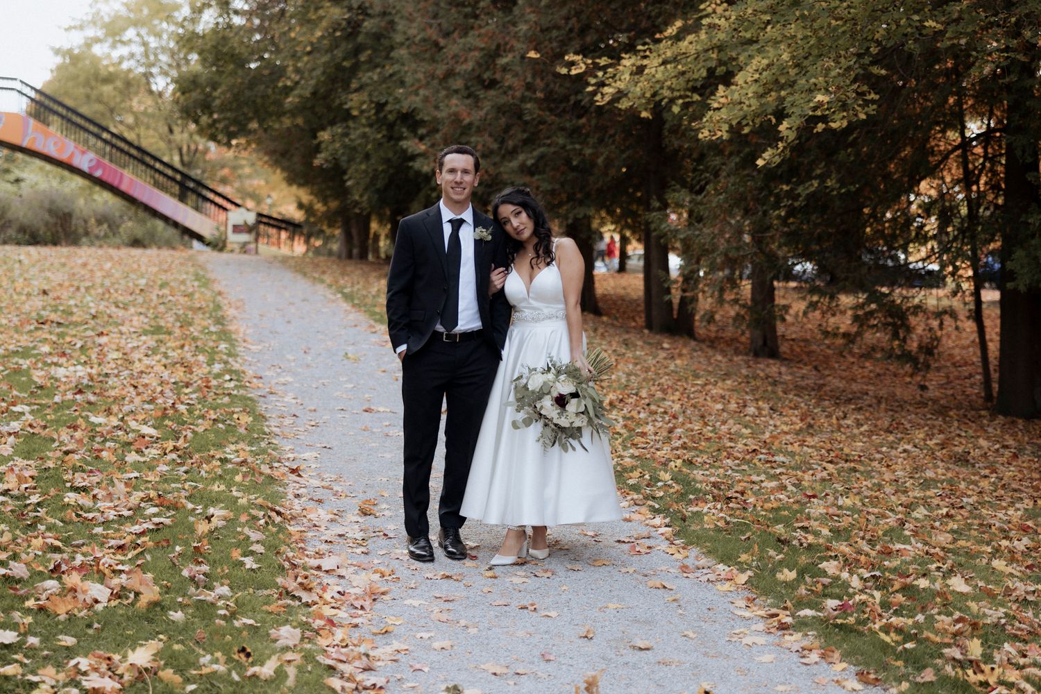 A wedding couple walks along a fall path covered in autumn leaves.