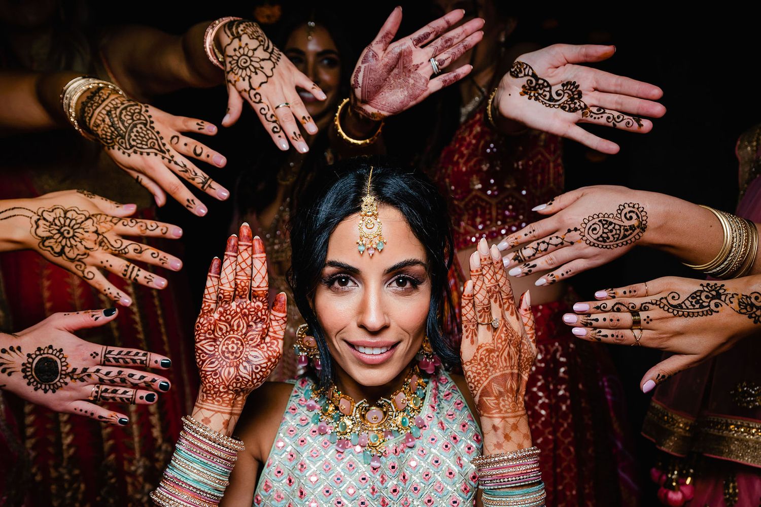 Traditional Indian bridal mehndi ceremony showing intricate henna designs on hands surrounding the elegant bride.