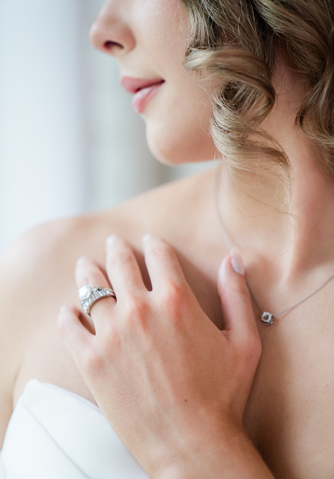 A close-up view showing a delicate engagement ring and necklace on fair skin with soft lighting.