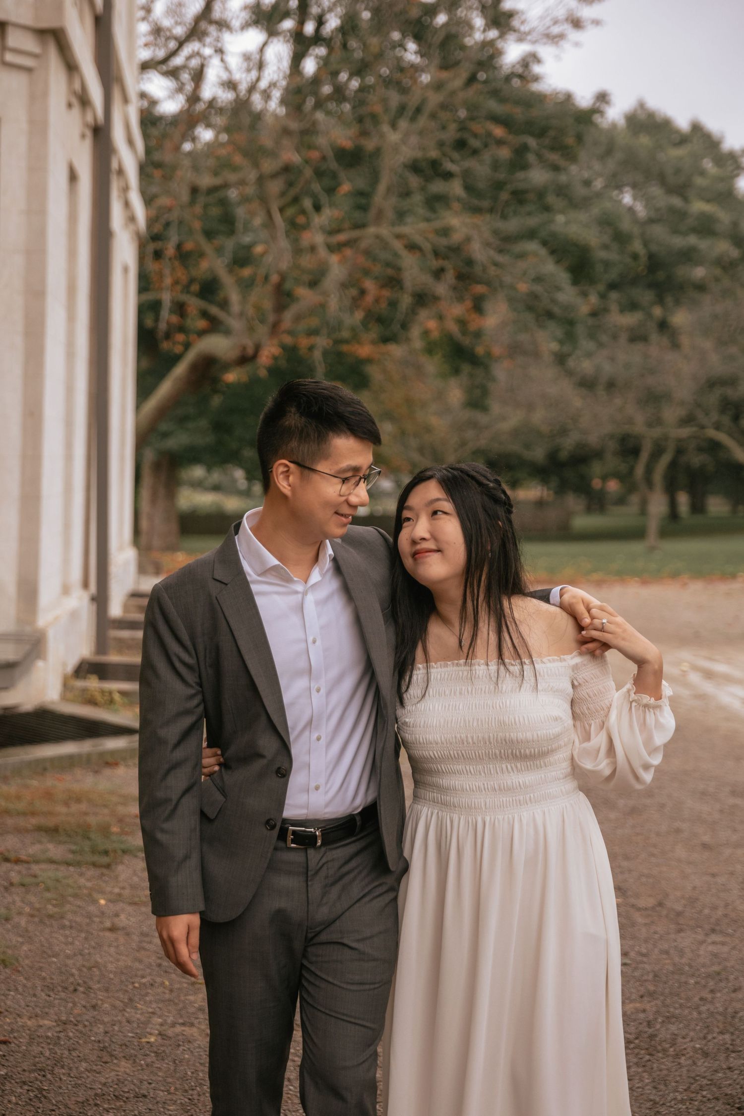 Couple in formal attire sharing a romantic moment while walking outside a historic building.
