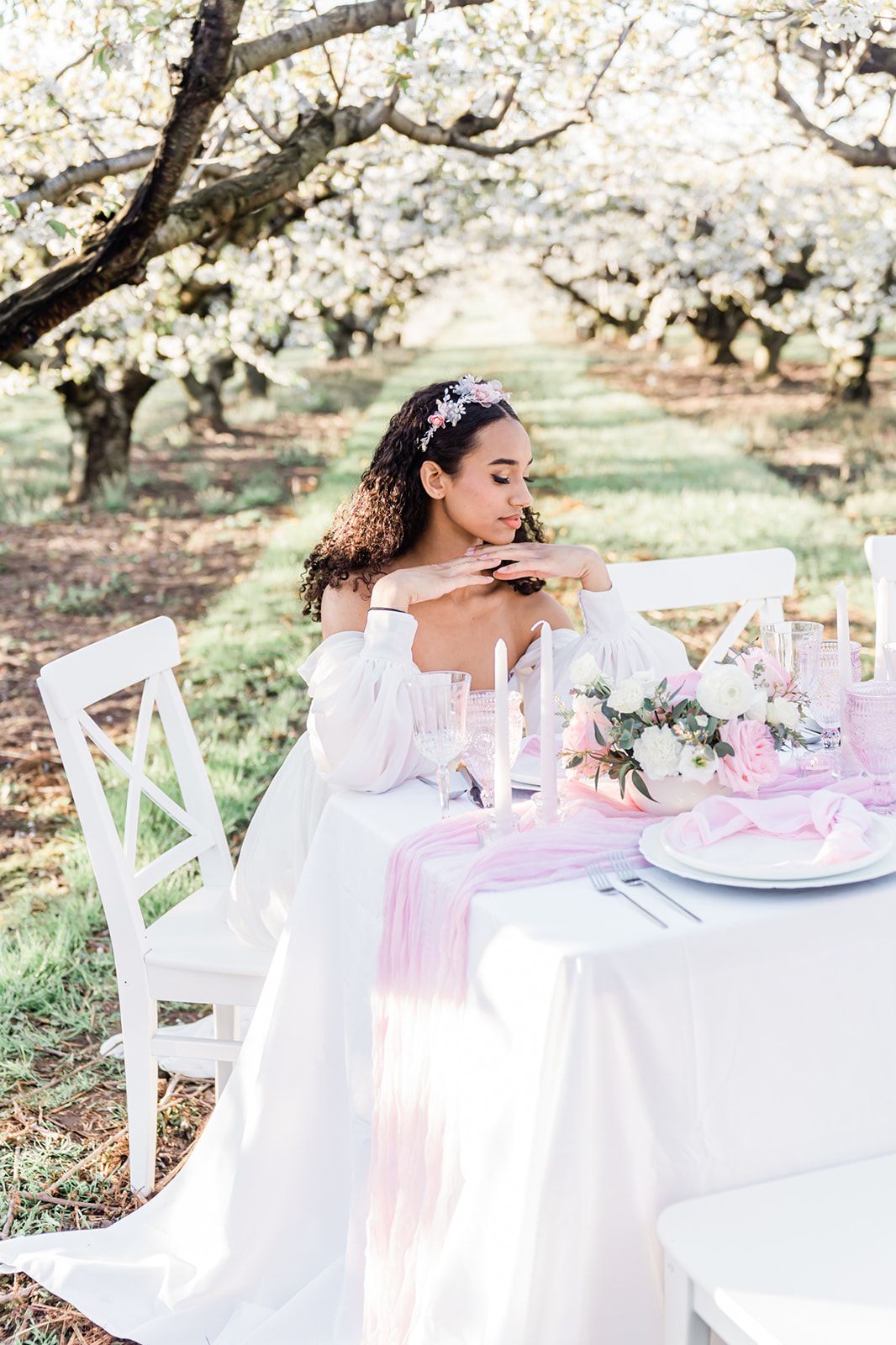 Romantic spring wedding table setting with pink runner and candles under blooming trees in an orchard garden.