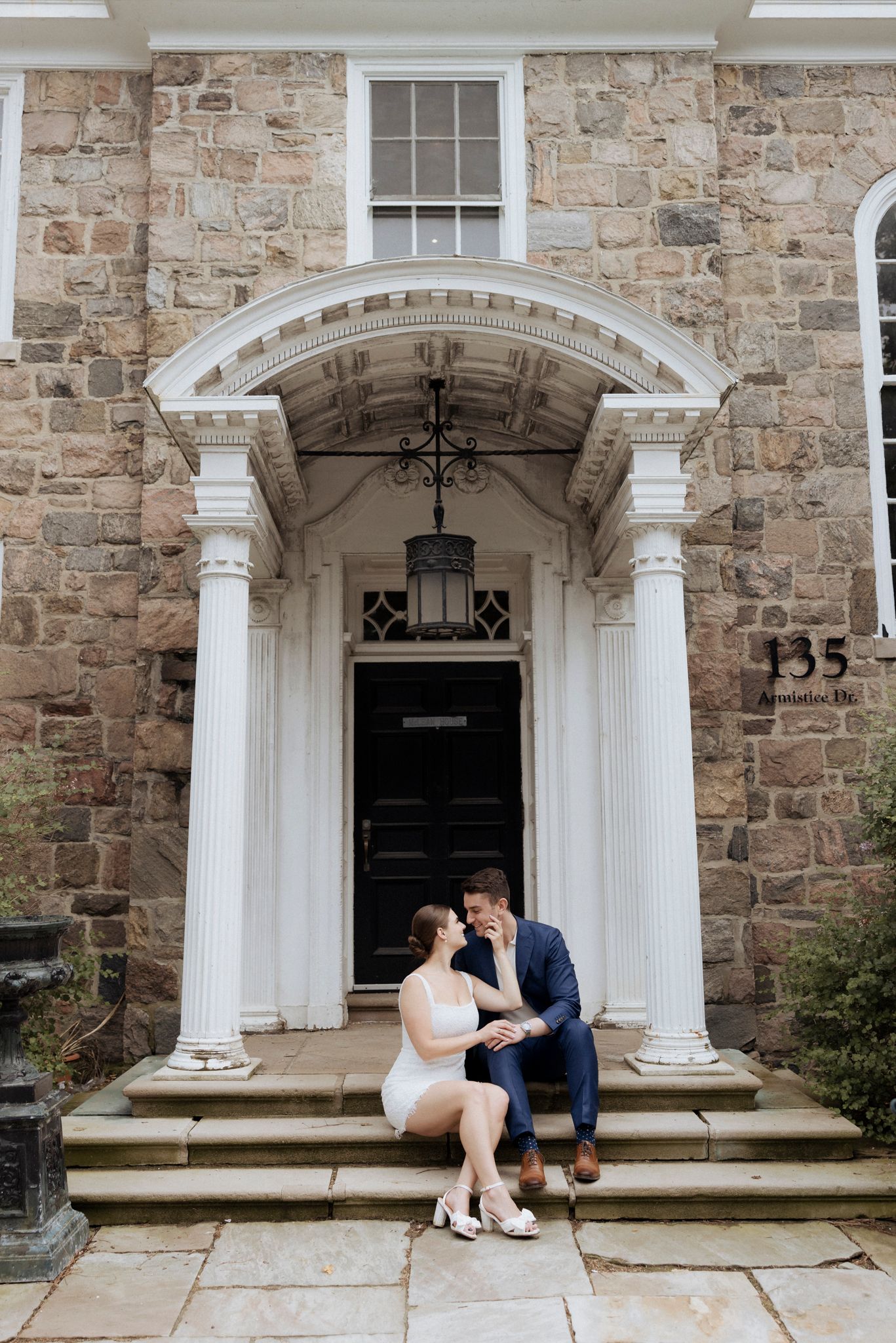 A couple sits together on stone steps under an elegant arched doorway entrance.