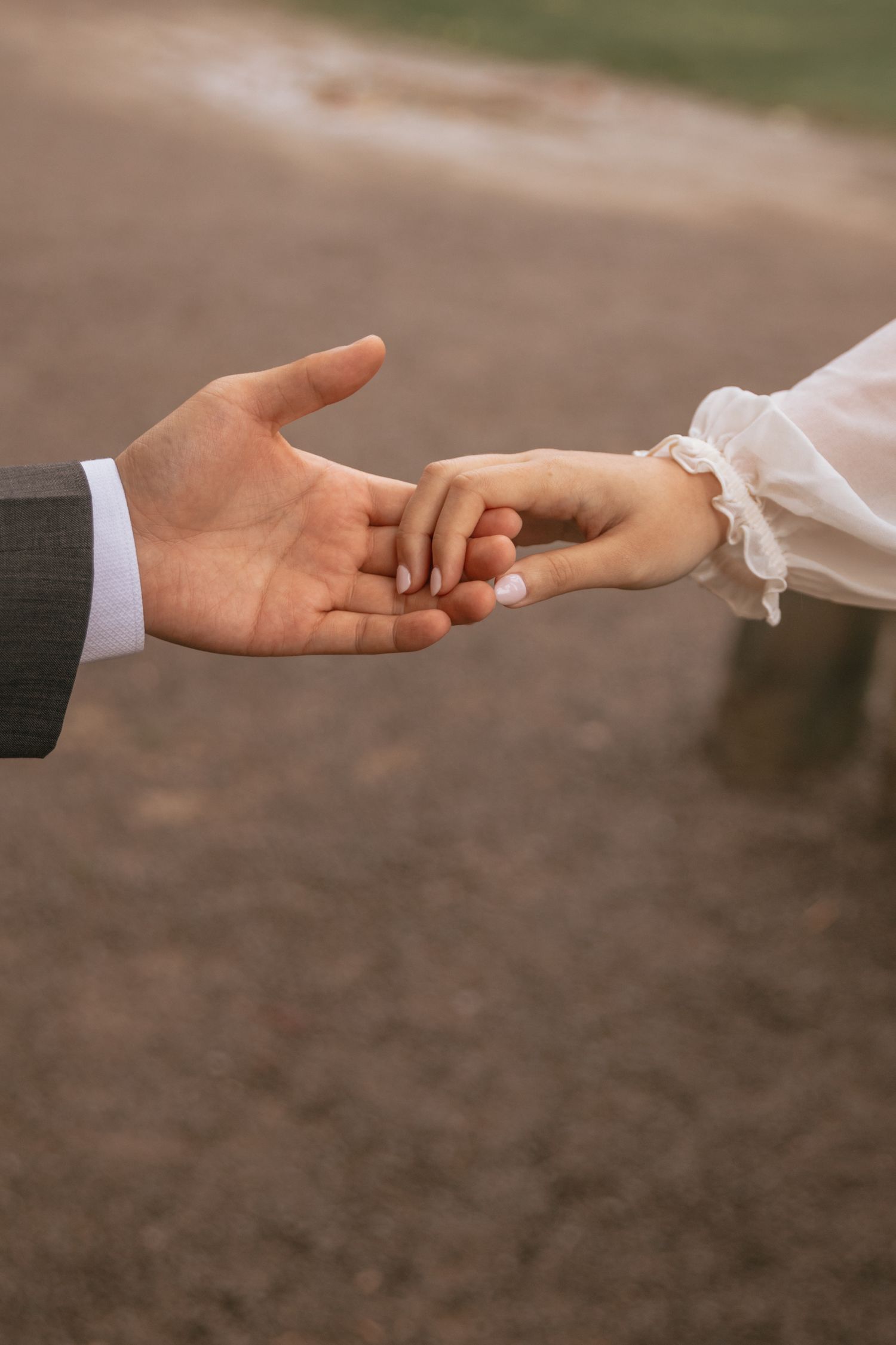 Two hands reach toward each other tenderly with one wearing a white sleeve and one wearing a dark suit sleeve.
