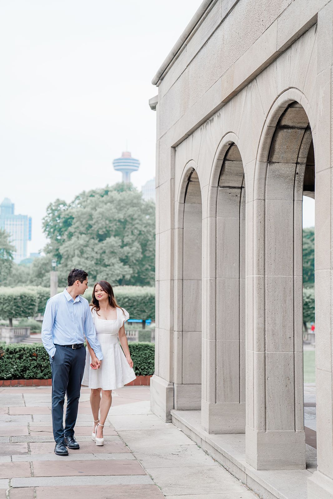 Couple walking together under stone archways with the Seattle Space Needle visible in the background.