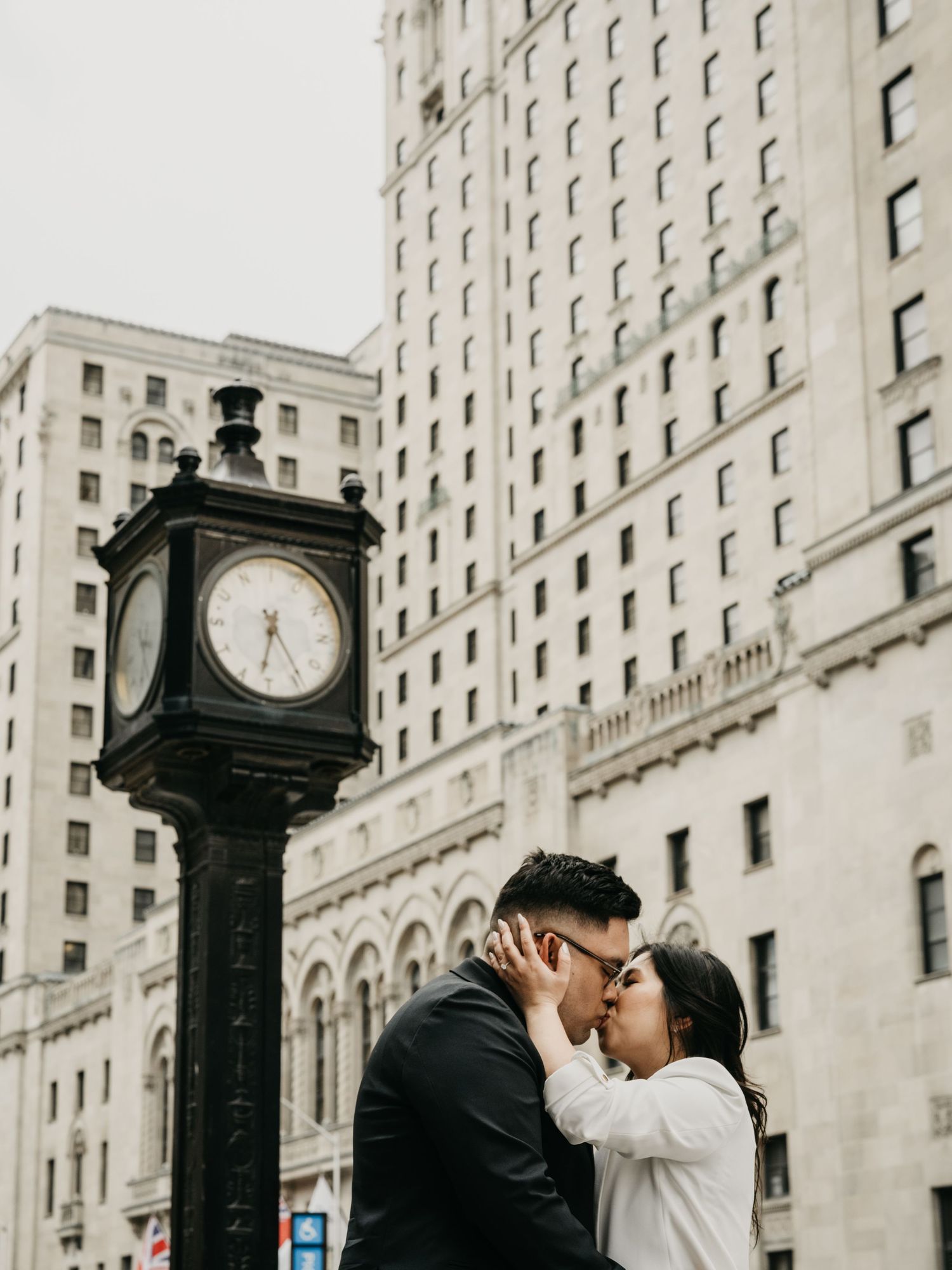 A romantic kiss in front of a vintage street clock and classic architecture in a city setting.