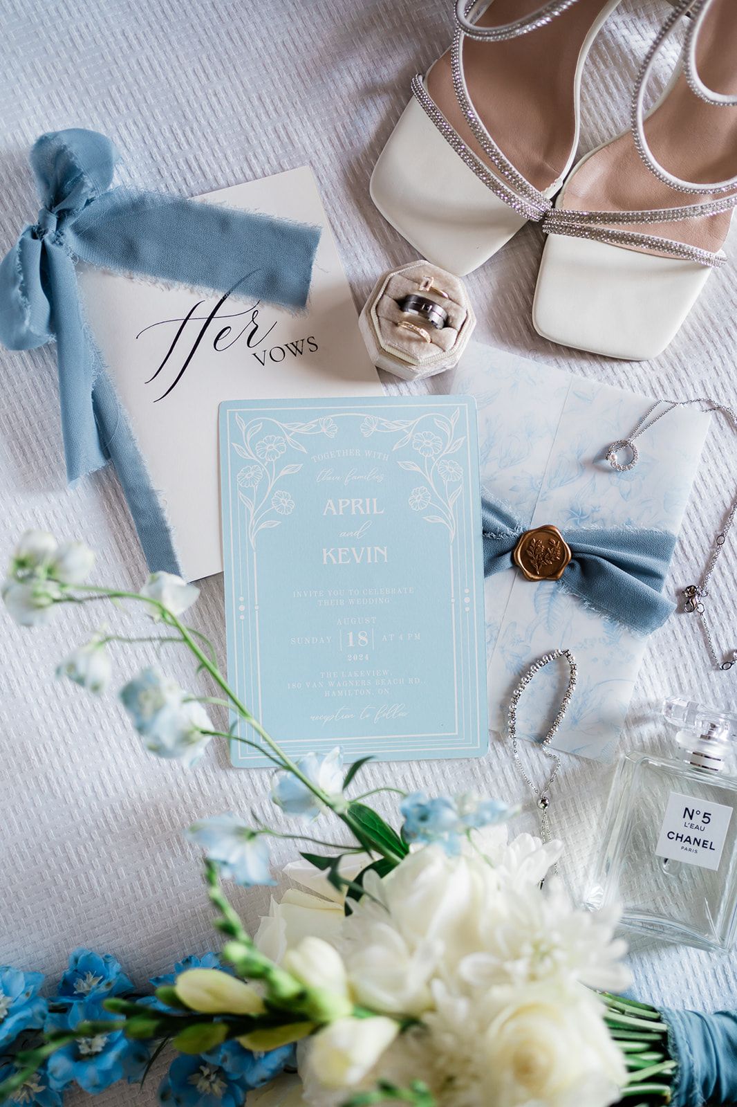 Wedding details including blue ribbons, white shoes, invitations and floral arrangements lay artfully arranged.