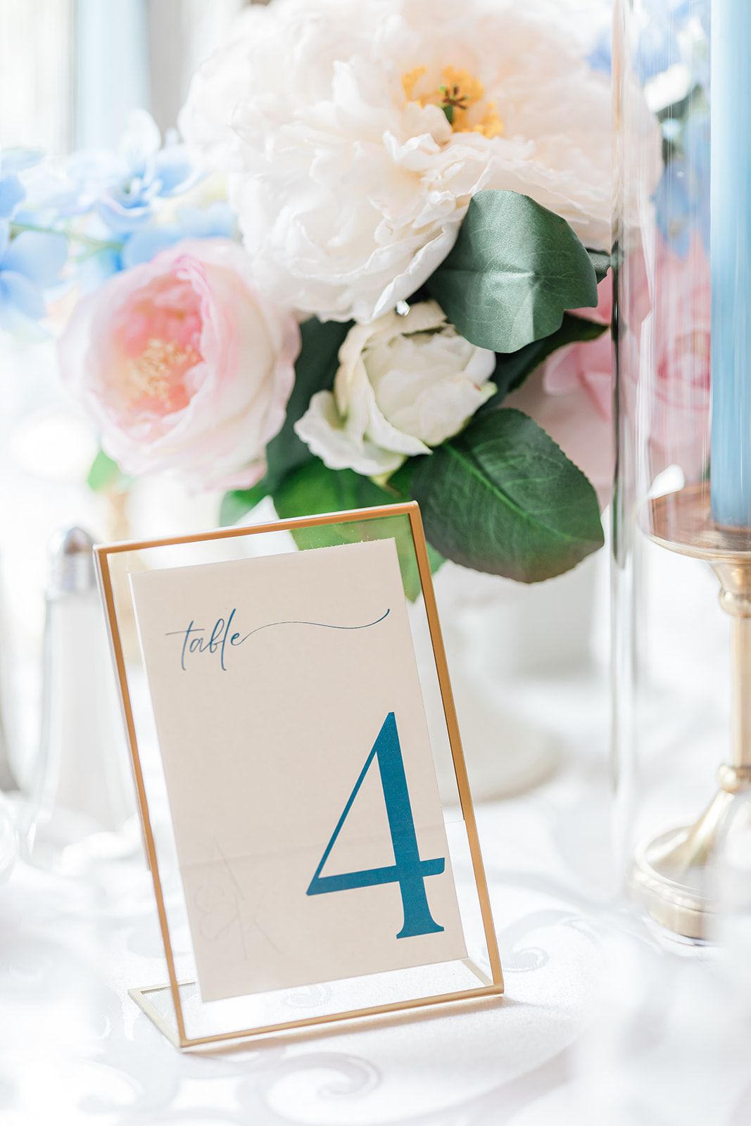 Elegant table number four display with soft pink and white flowers in a glass vase against a light background.