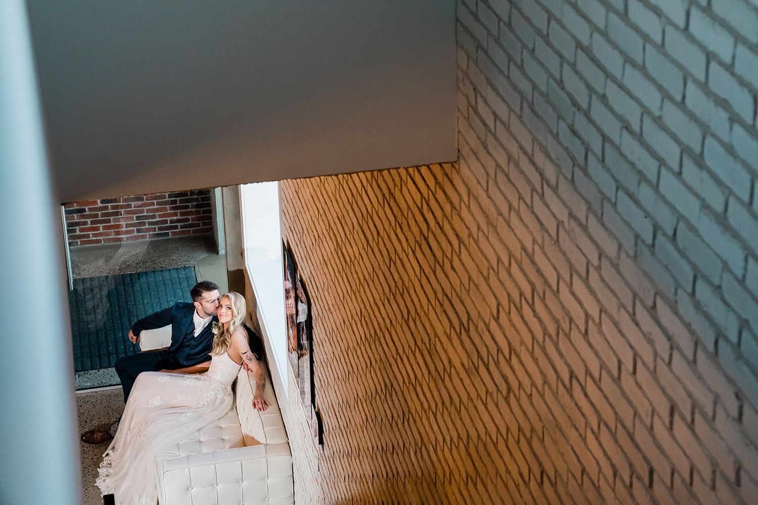 A couple relaxes on a white sofa against a textured brick wall in an intimate moment.