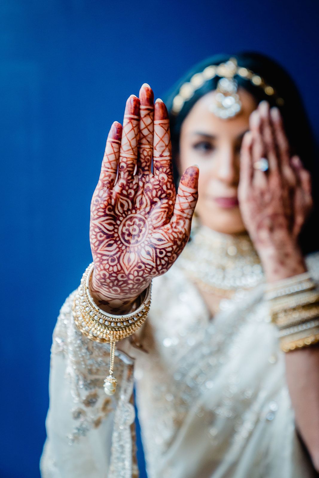 Intricate henna design on palm with traditional Indian bridal jewelry and attire against blue background.
