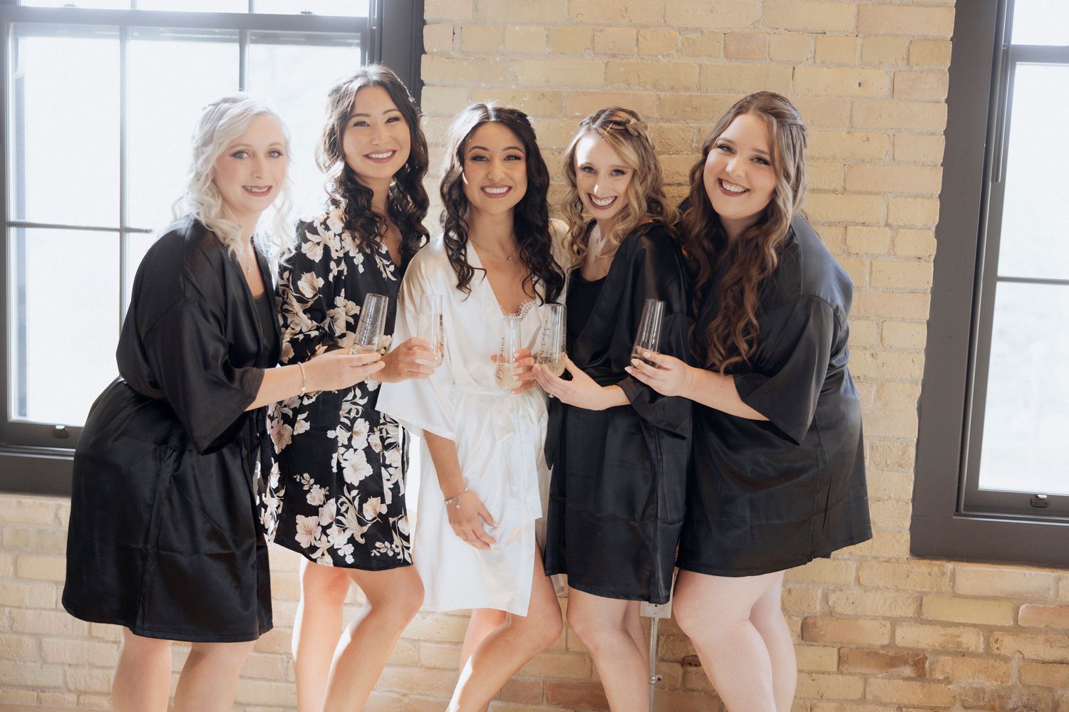 A bridal party in black robes celebrates together in a bright indoor space.