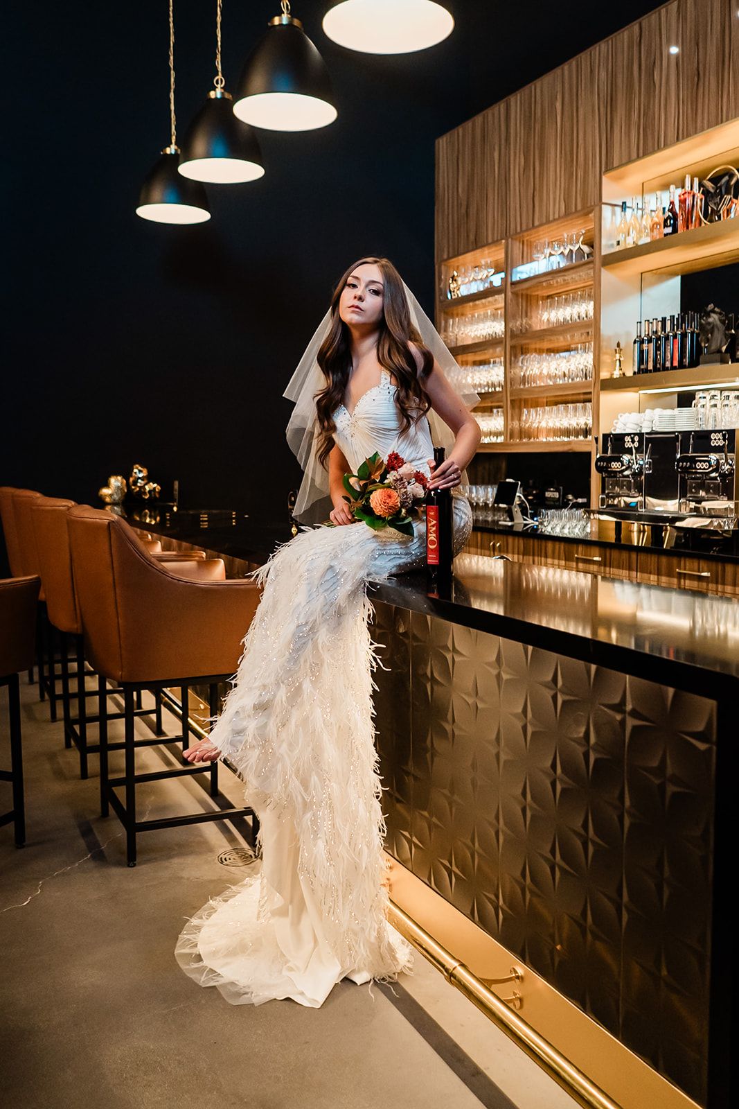 Fashion photograph in modern bar setting with dramatic pendant lighting and gold metallic accents.