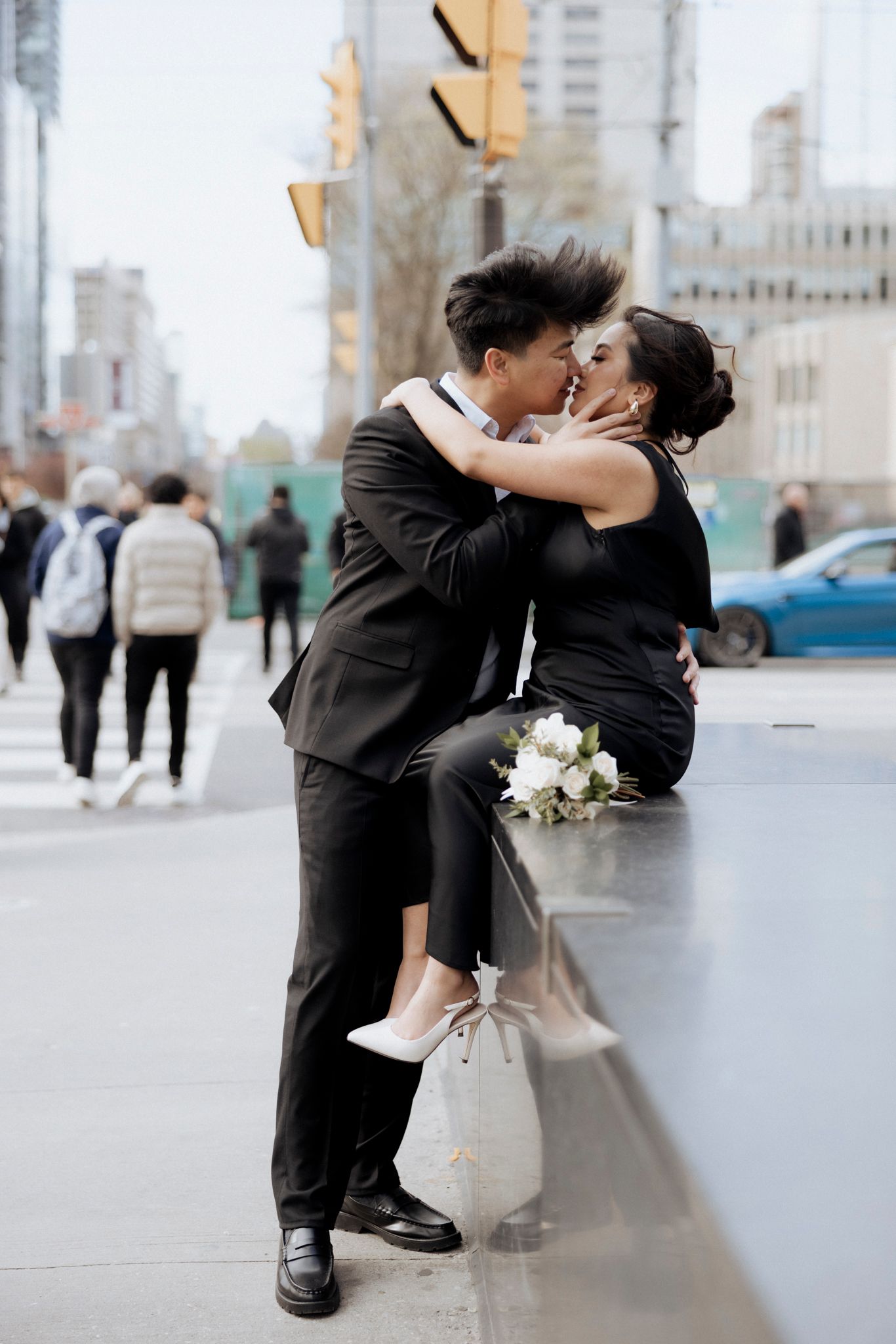 Couple in formal wear sharing a romantic moment by a city street with a white bouquet.