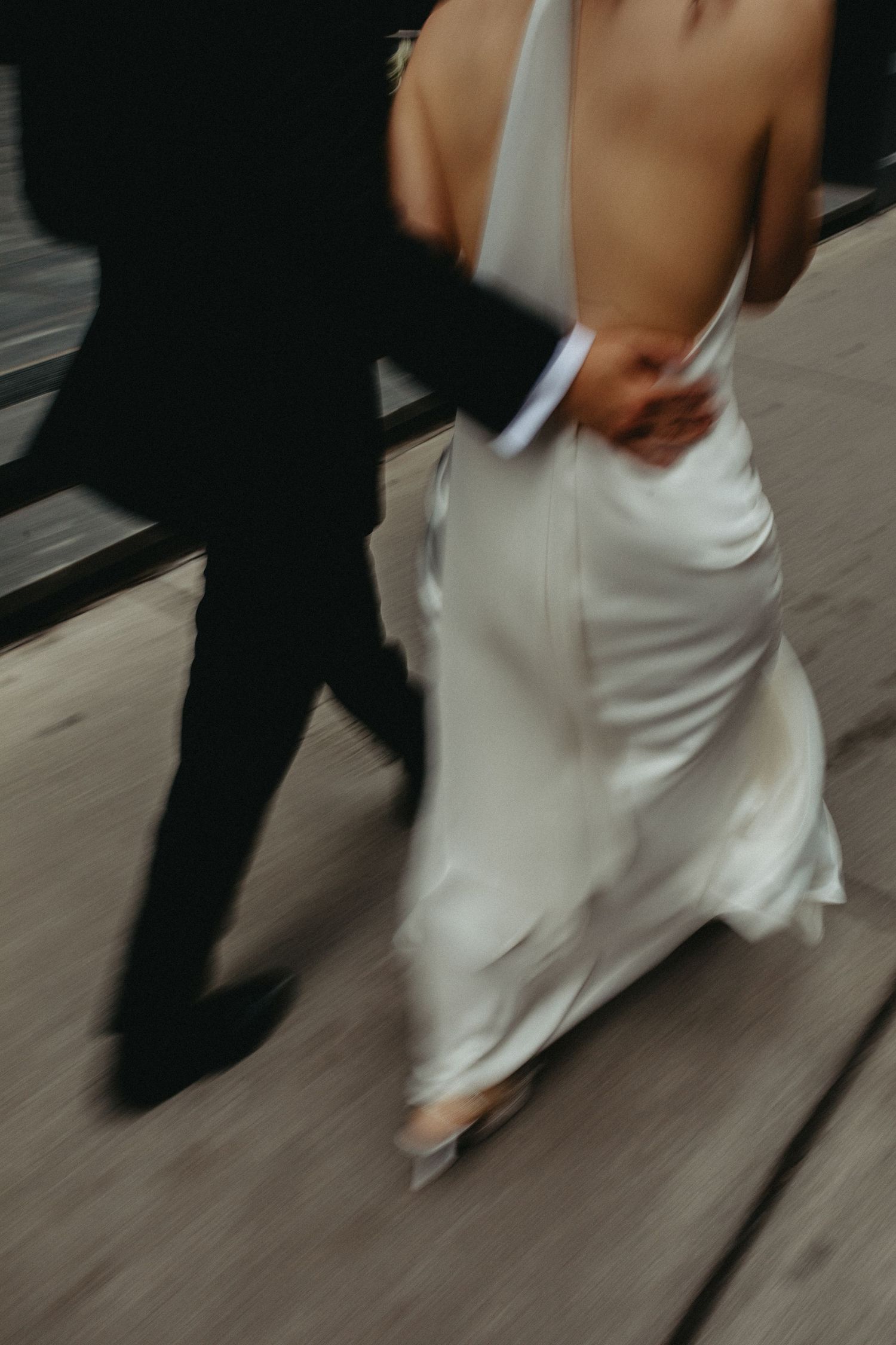 A couple in wedding attire walking together with a blurred artistic motion effect on a wooden deck.