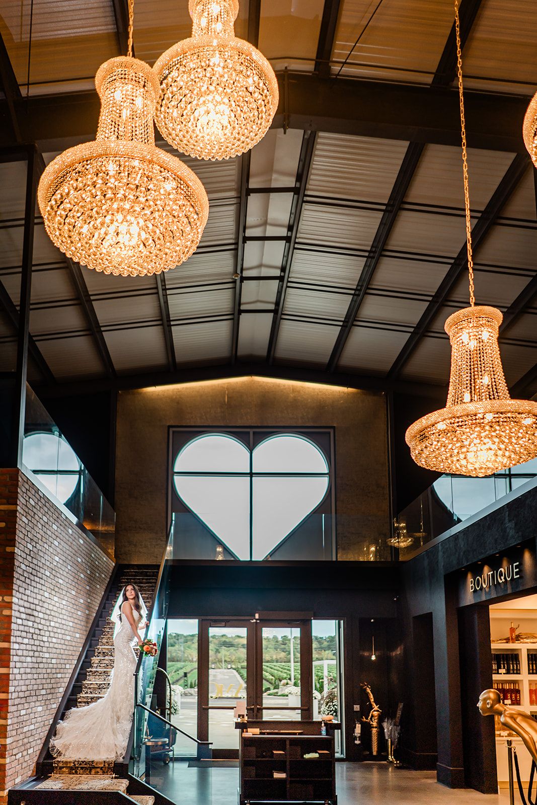 Crystal chandeliers illuminate an industrial venue interior with exposed beams and a heart-shaped window feature.