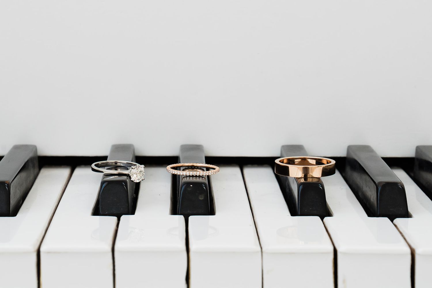 Three elegant wedding rings displayed on black and white piano keys in a minimalist arrangement.