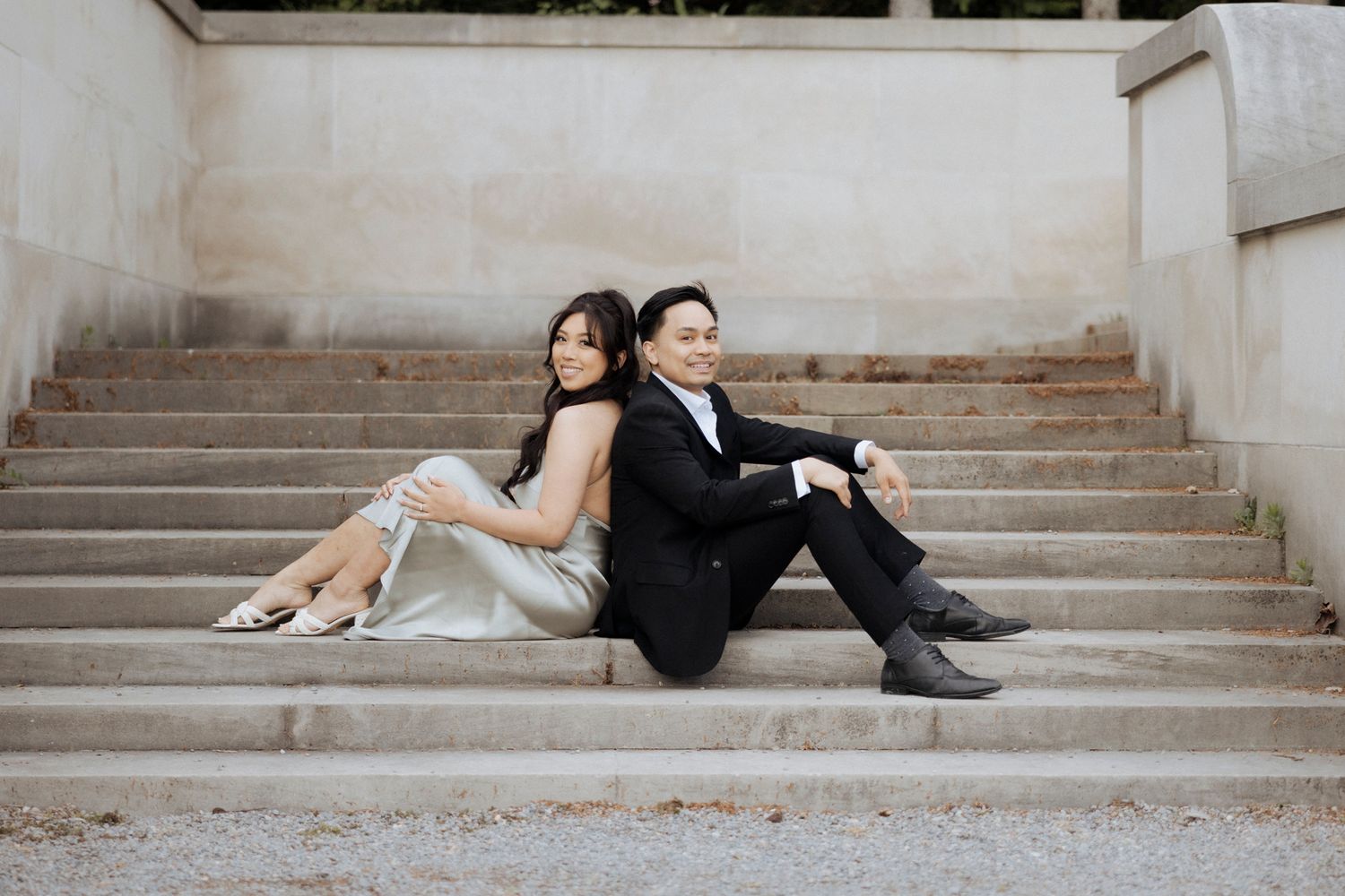 Couple sitting back to back on concrete steps in formal attire.