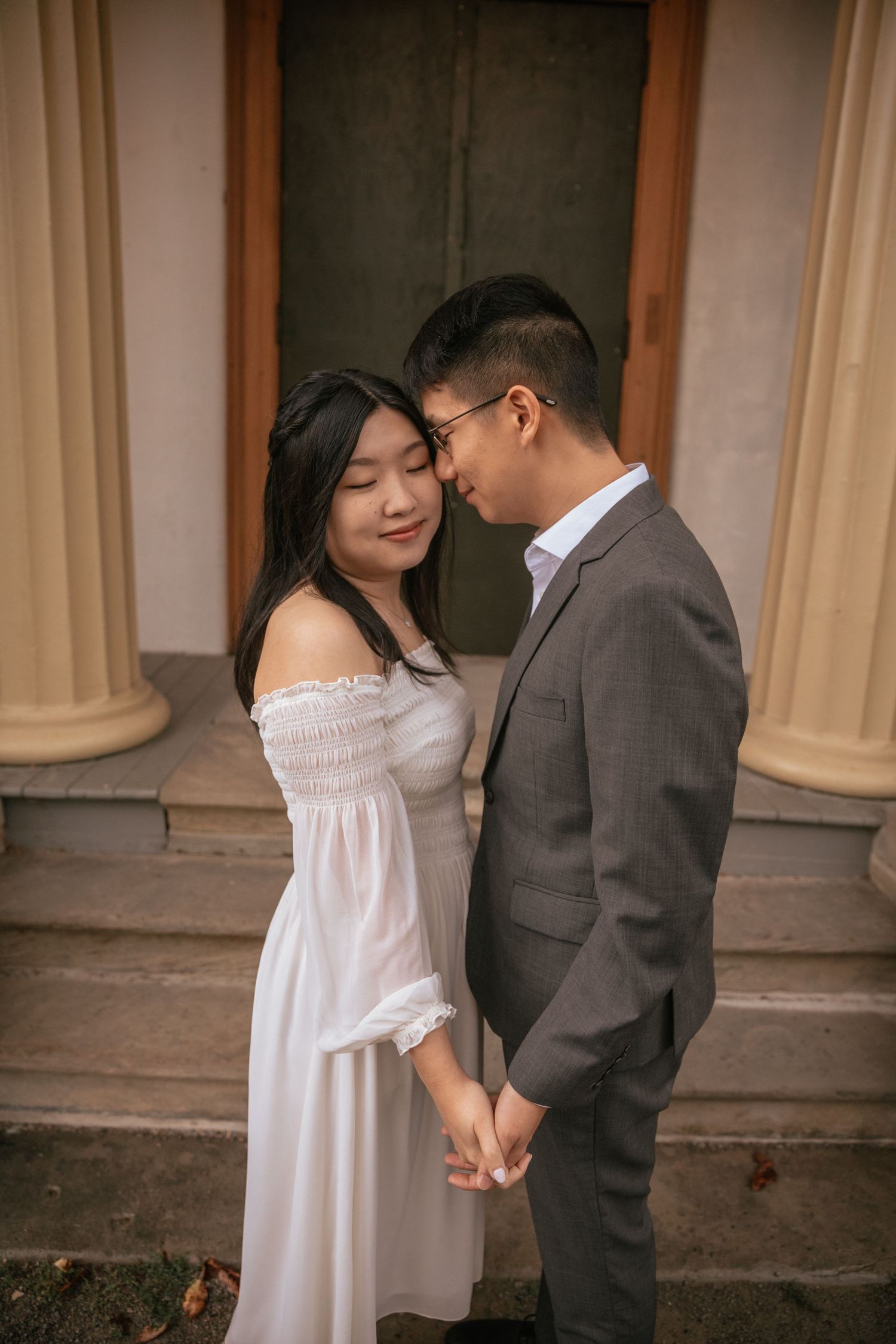 A romantic couple in formal attire share an intimate moment while holding hands on stone steps.