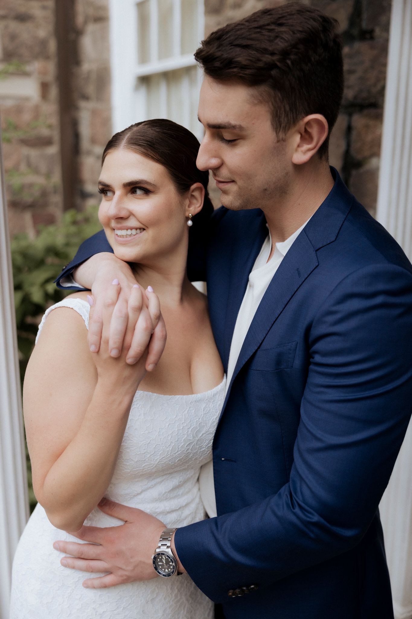 An elegant couple poses intimately against a white stone column in formal attire.