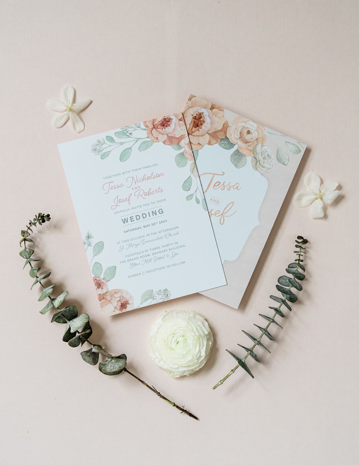 Elegant floral wedding invitation suite with soft pink roses and eucalyptus leaves styled with white flowers and greenery.