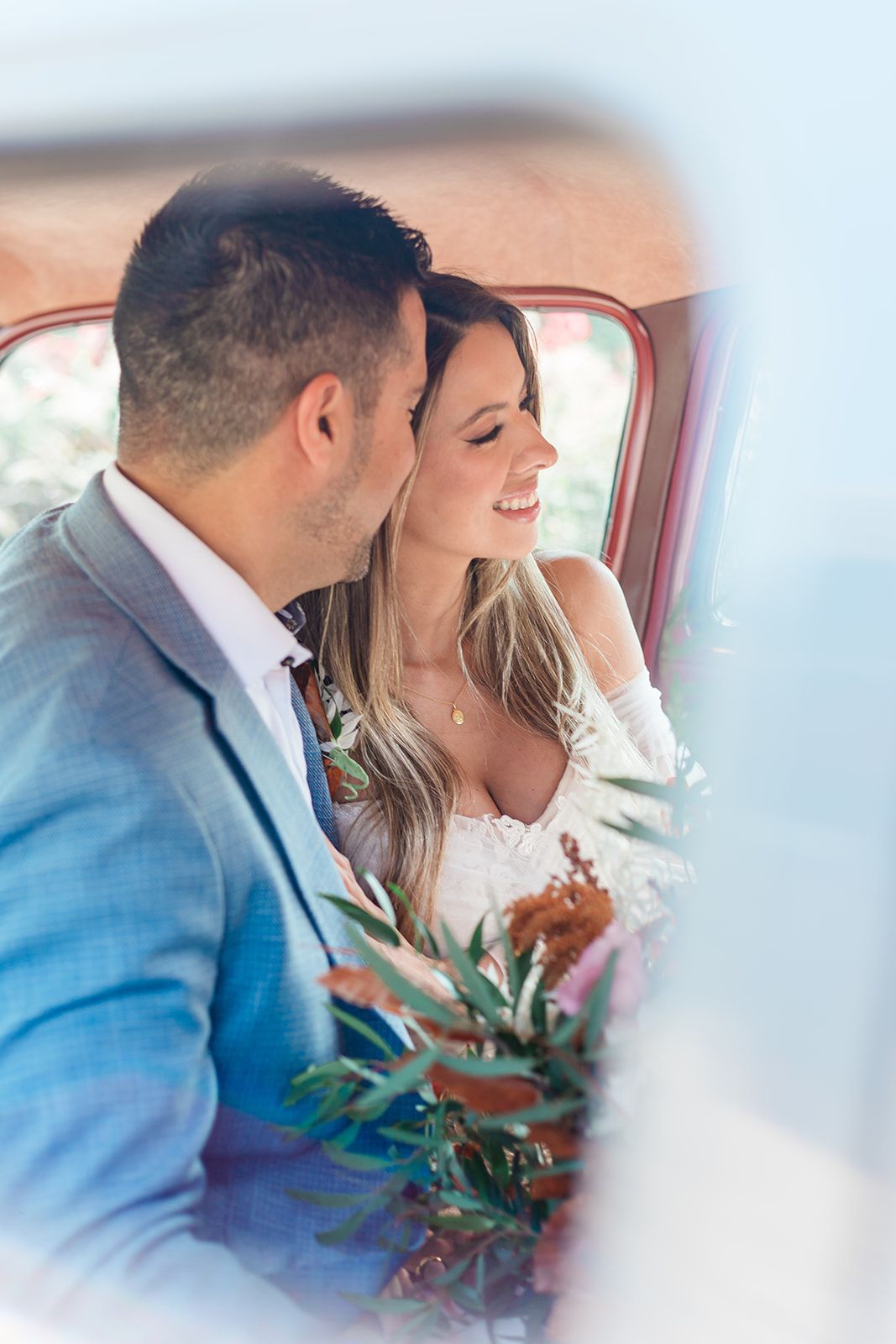 A romantic moment captured inside a vintage car as newlyweds share a tender moment with greenery and soft lighting.