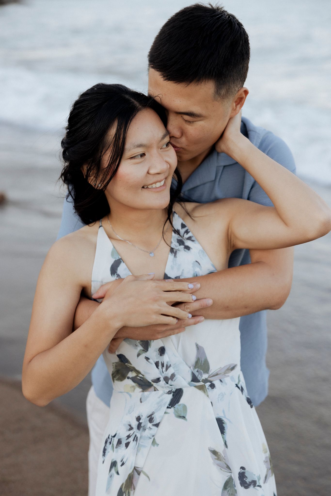 Romantic couple embracing at sunset while showing off engagement ring.