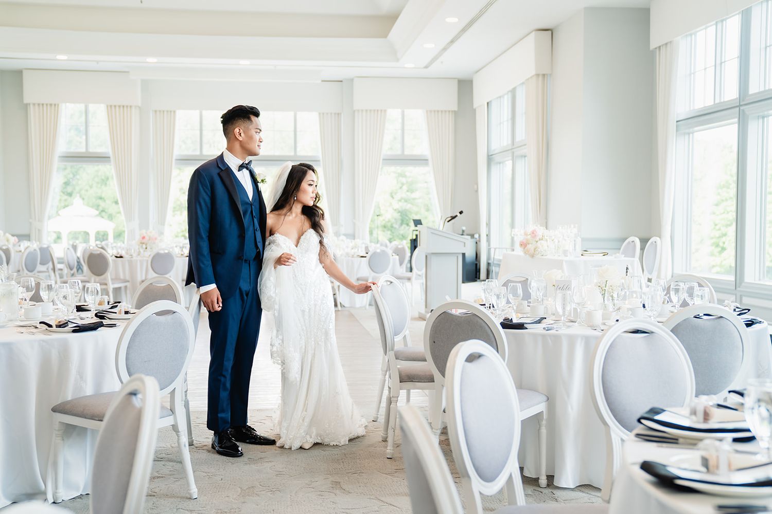 Elegant white wedding reception hall with modern place settings and chairs arranged around circular tables.