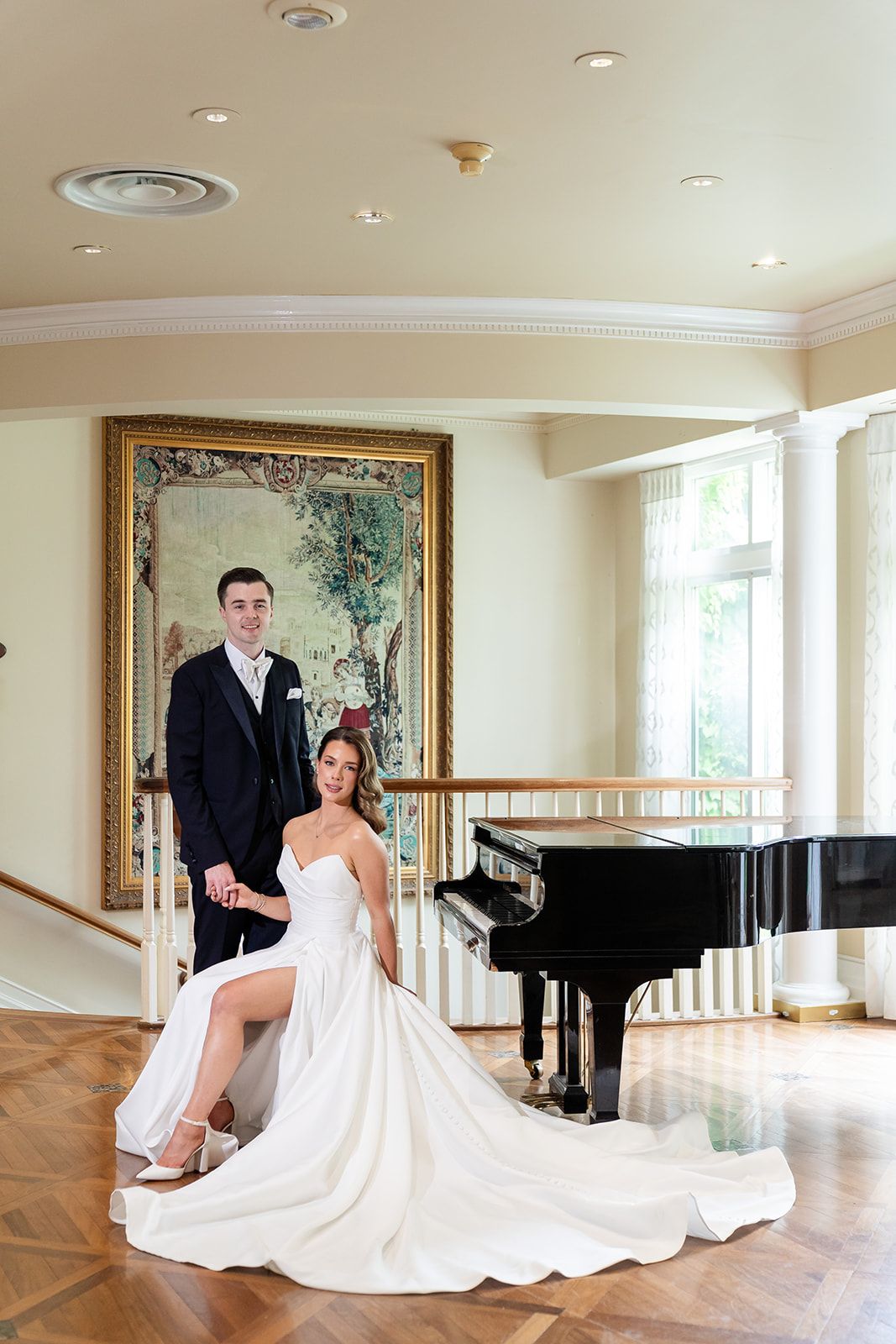 Formal wedding portrait in an elegant room with a grand piano and framed artwork.