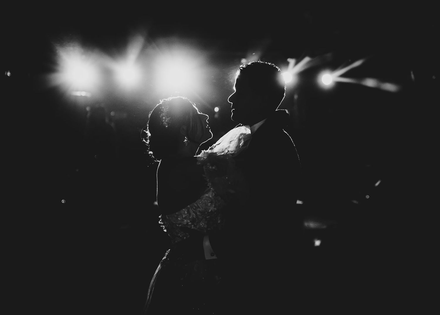 A silhouetted couple embraces on a dark dance floor with dramatic backlighting creating a romantic atmosphere.