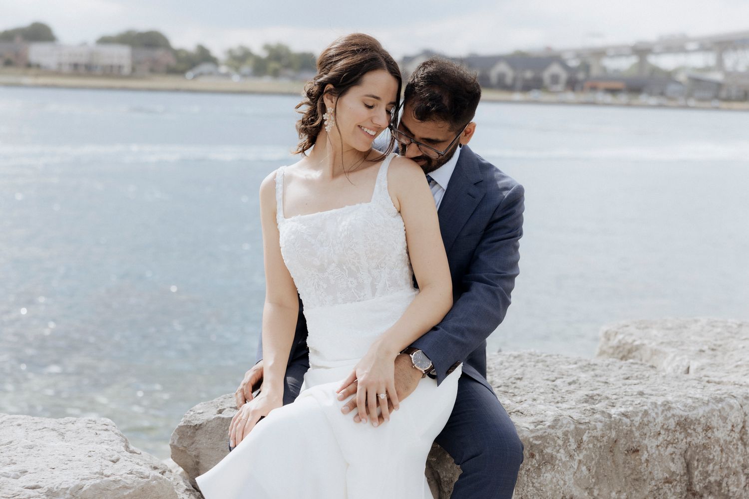 A couple poses intimately on coastal rocks with water in the background.