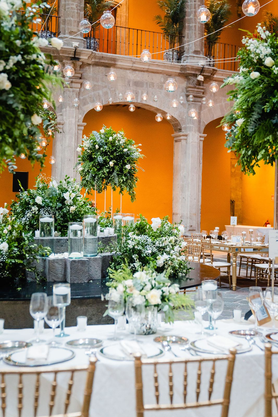 Elegant wedding reception venue with orange walls, stone arches, and hanging lights adorned with lush white floral arrangements.