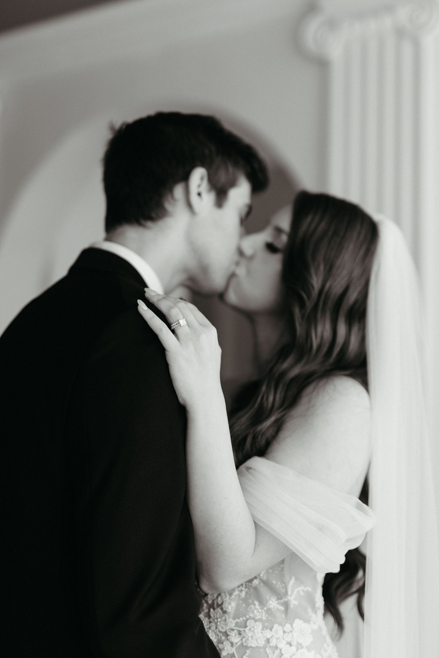 A romantic black and white wedding photo captures a tender kiss between newlyweds.
