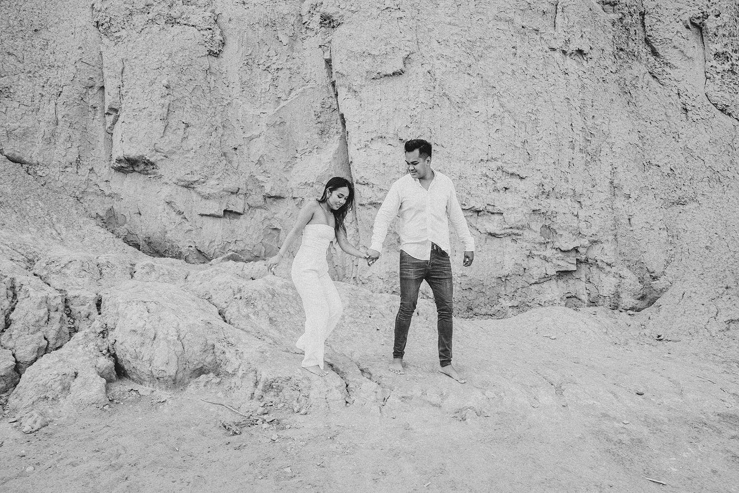 A couple poses playfully on a rocky beach cliff in black and white.