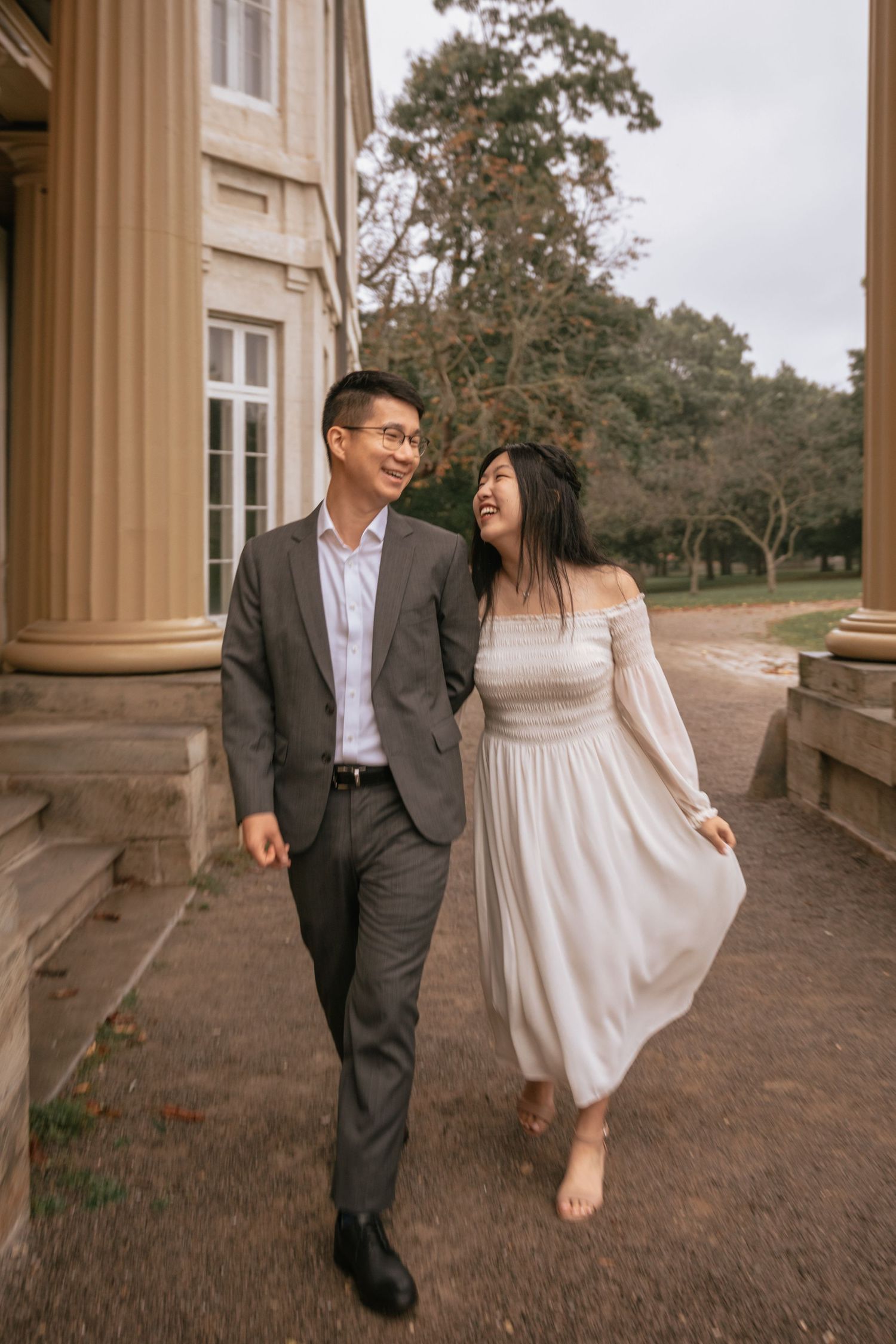 A romantic couple walking together outside a historic building with elegant columns and stone architecture.