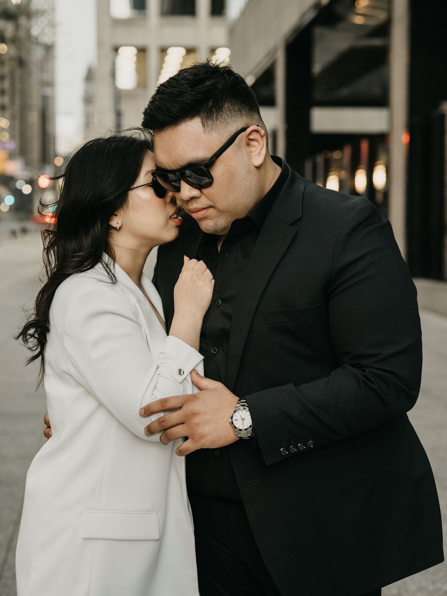A couple in contrasting black and white outfits share an intimate moment together on a city street.