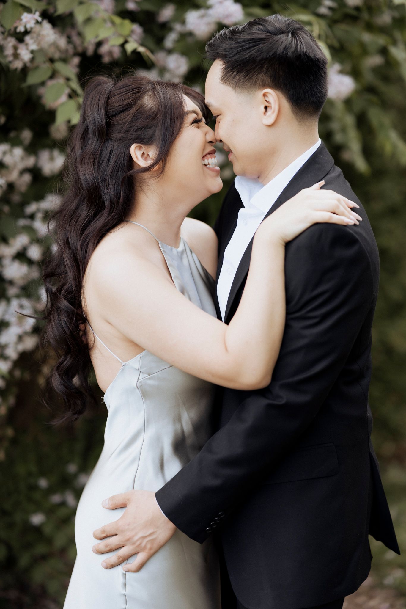 A couple shares an intimate moment in formal attire against a backdrop of spring blossoms.