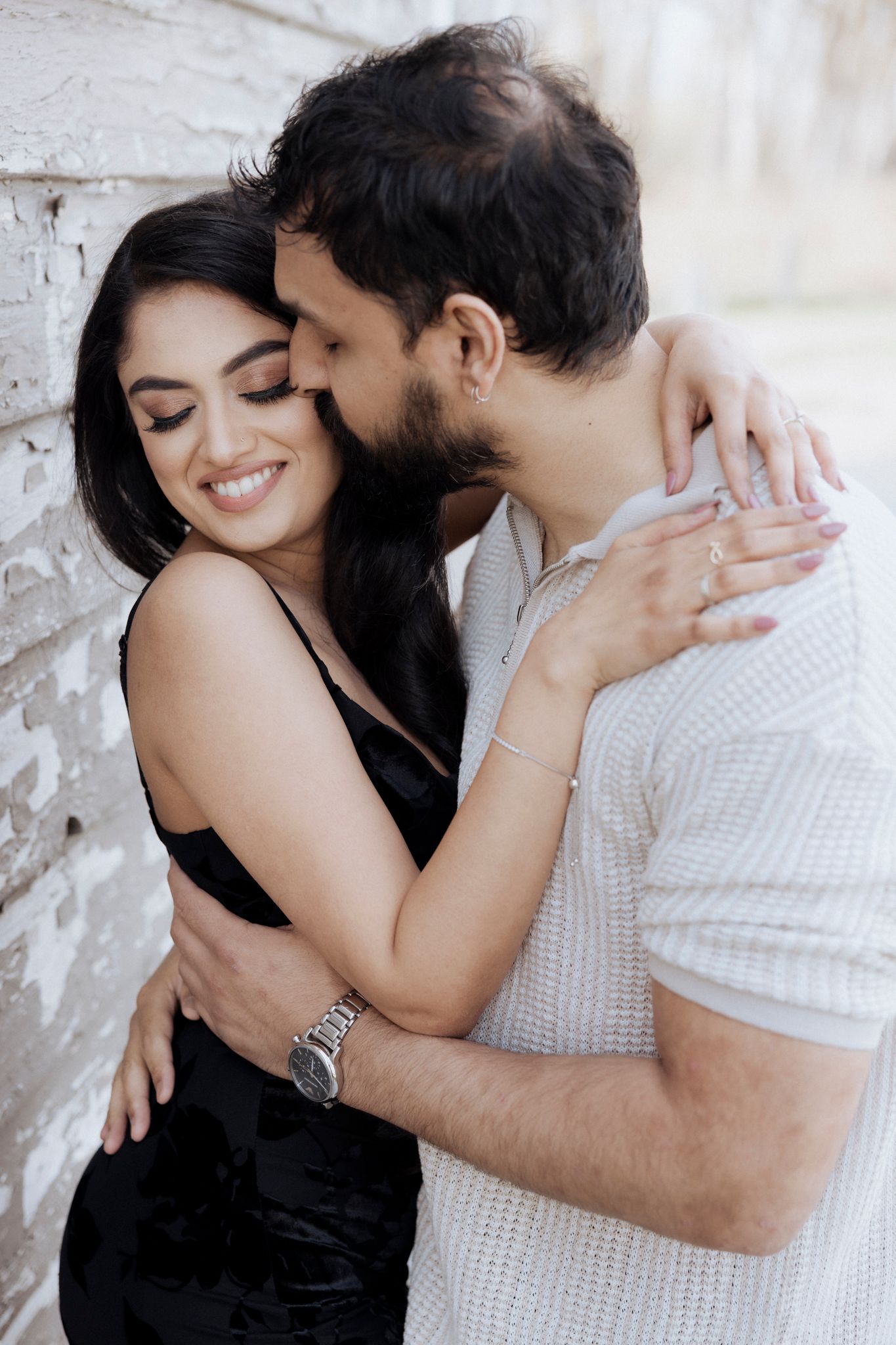A tender embrace against a white brick wall capturing a romantic moment.