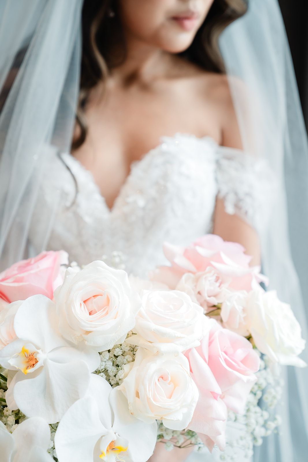 A beautiful wedding bouquet featuring pink and white roses with white orchids against a soft bridal gown background.