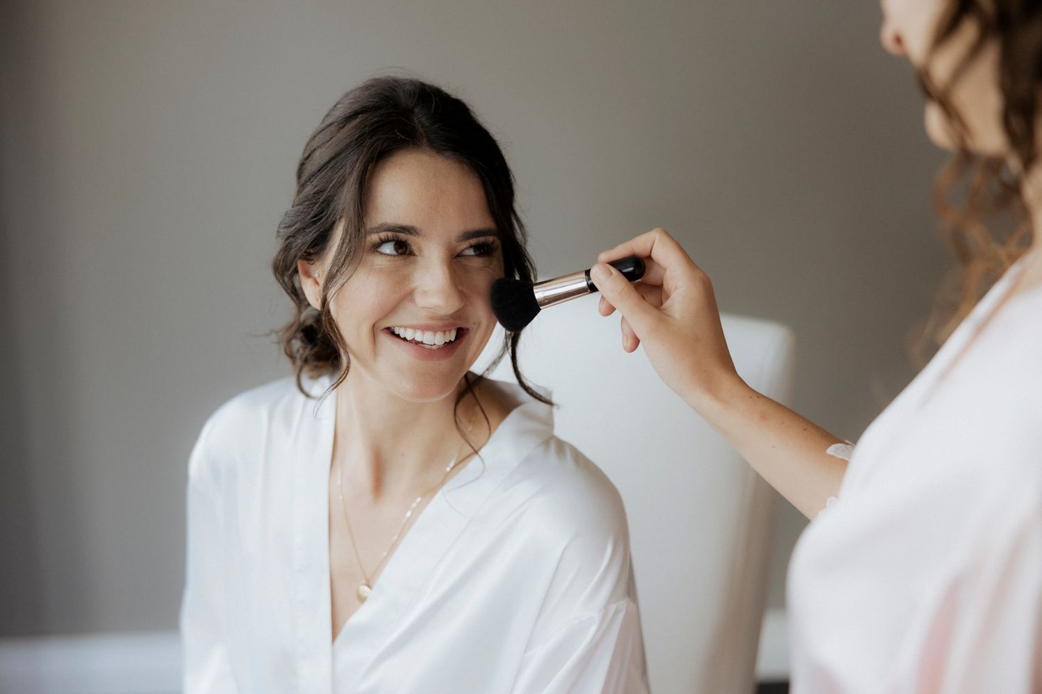 Person getting hair styled in white robe during wedding preparation.